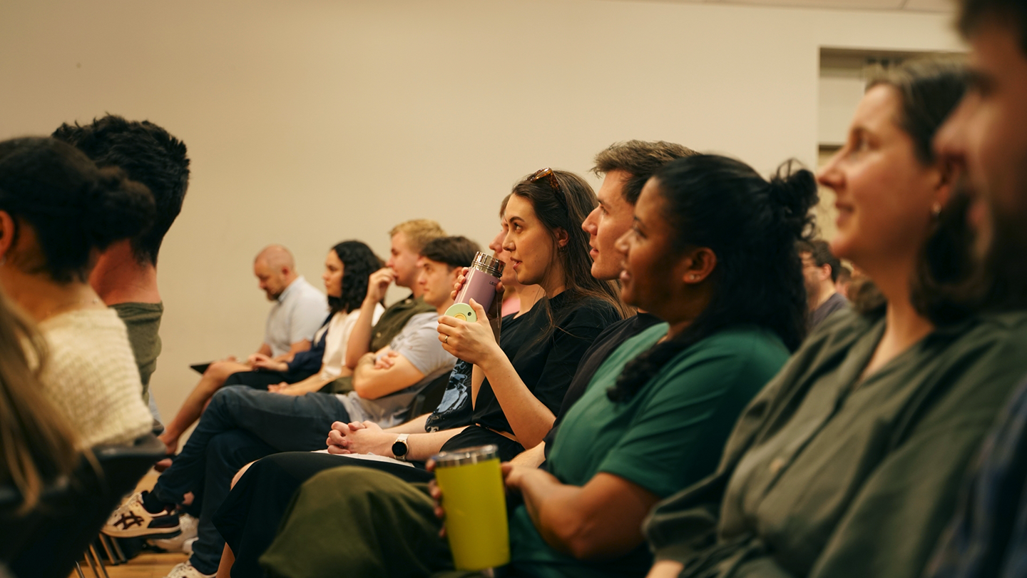 Audience members seated in rows listening to a speaker in an indoor event.