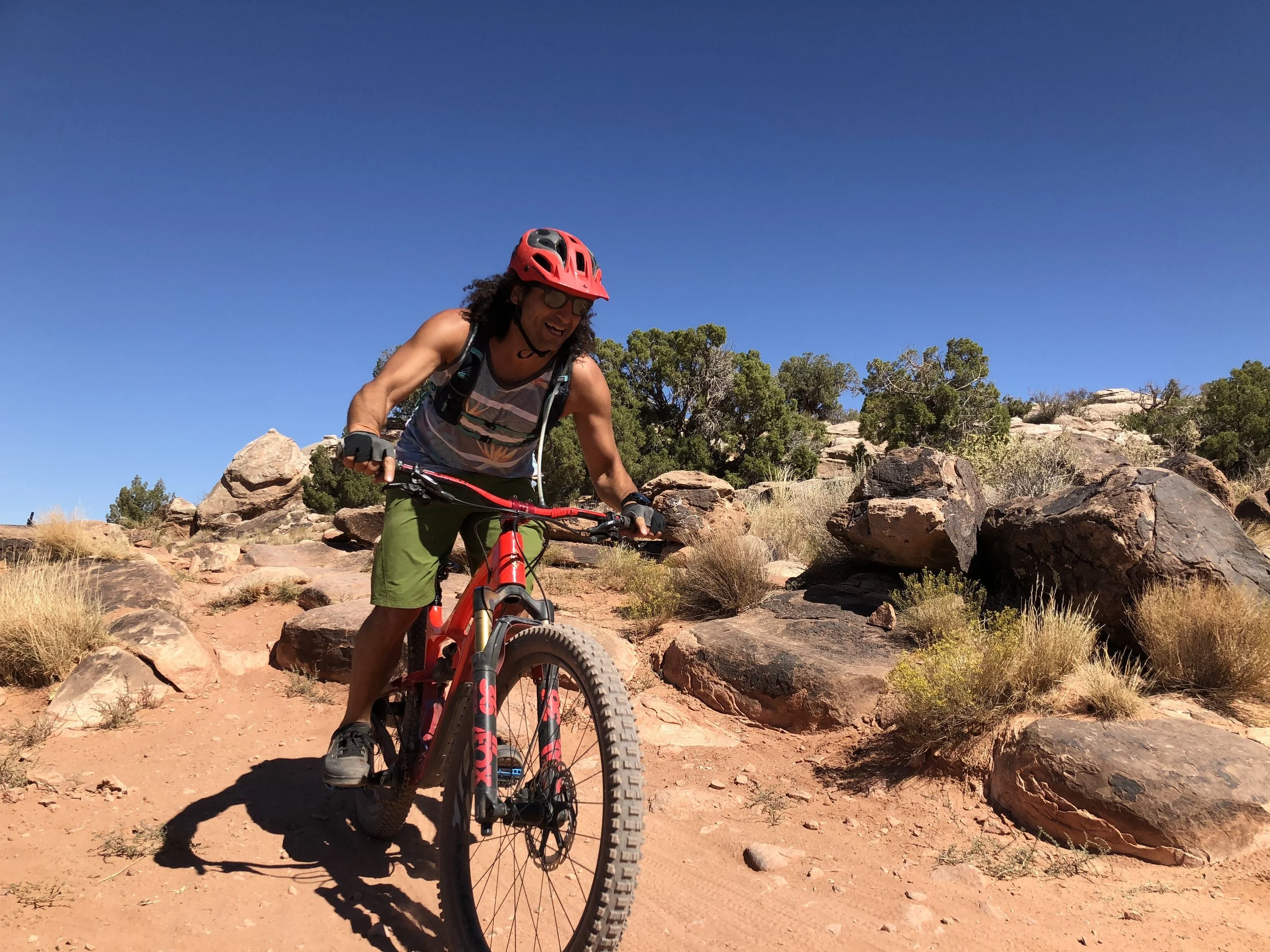 Woman hiking on a trail carved into red rock cliffside, with a backpack, surrounded by trees and mountains in the distance.