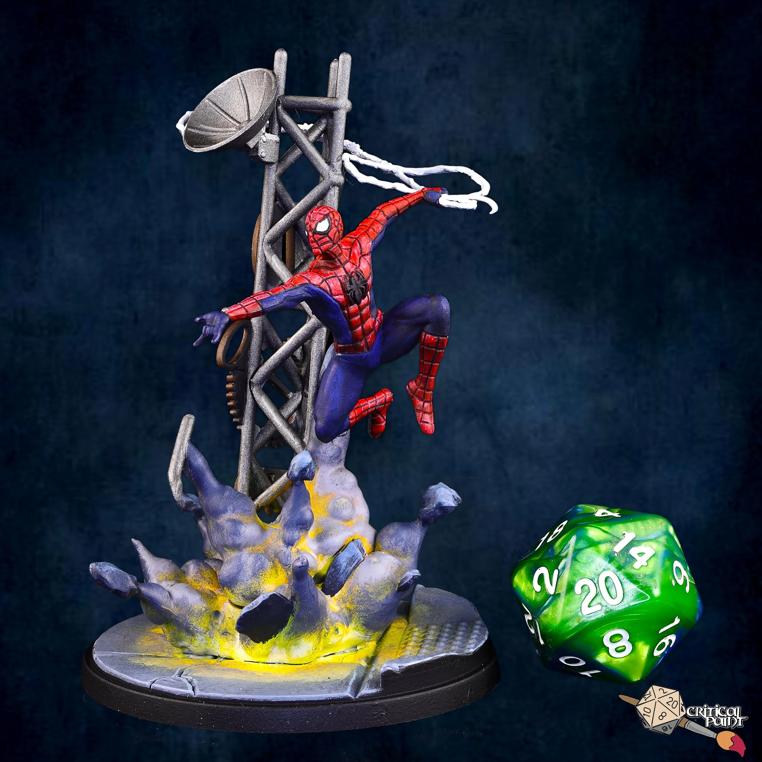 A miniature statue of Spider-Man hanging from a metallic tower with a white web. The statue is on a round base painted with yellow and purple accents. A green 20-sided die is partially visible at the bottom right corner.