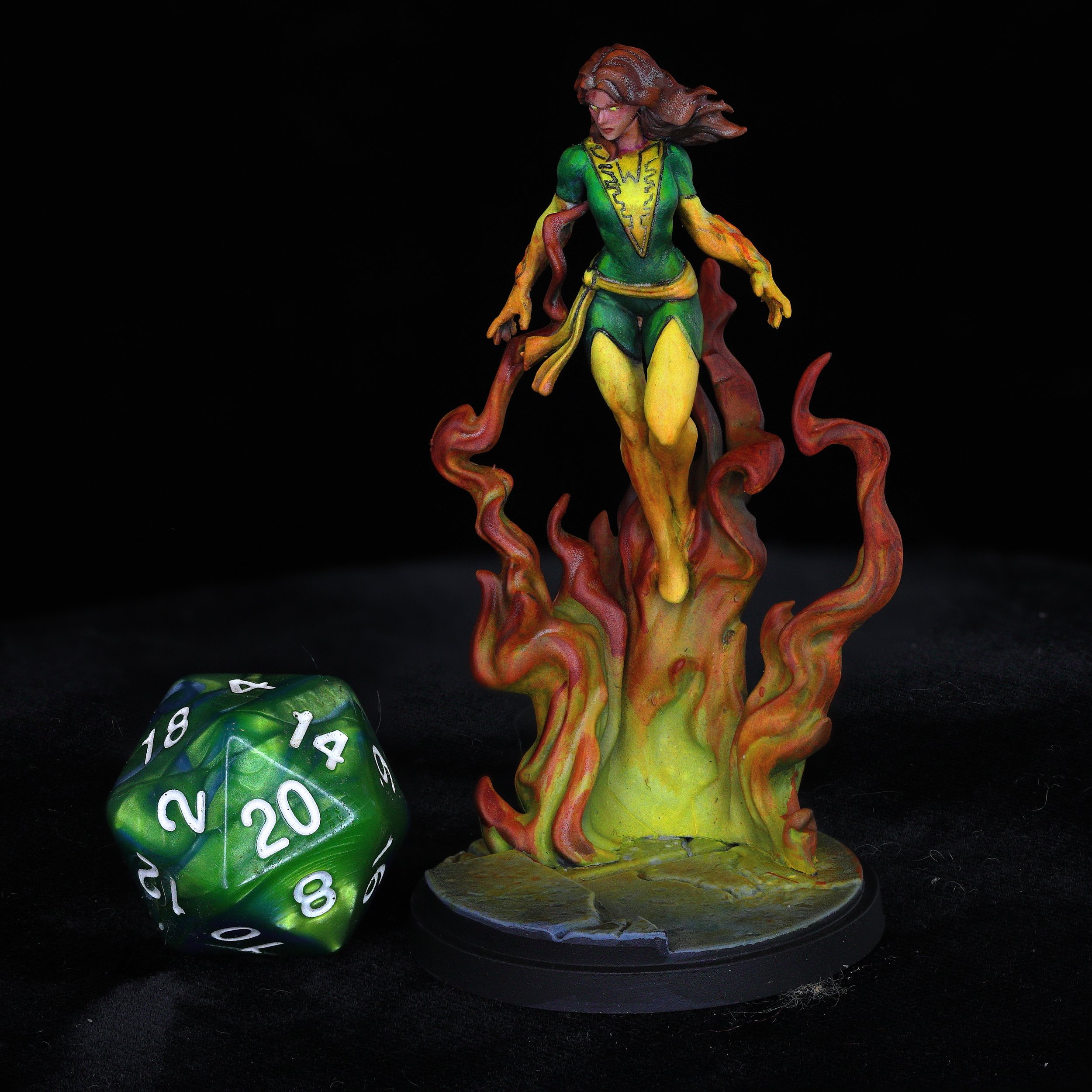 Colorful fantasy sculpture of a woman with flowing hair, surrounded by swirling tendrils, placed on a black background, with a green and black polyhedral die nearby.