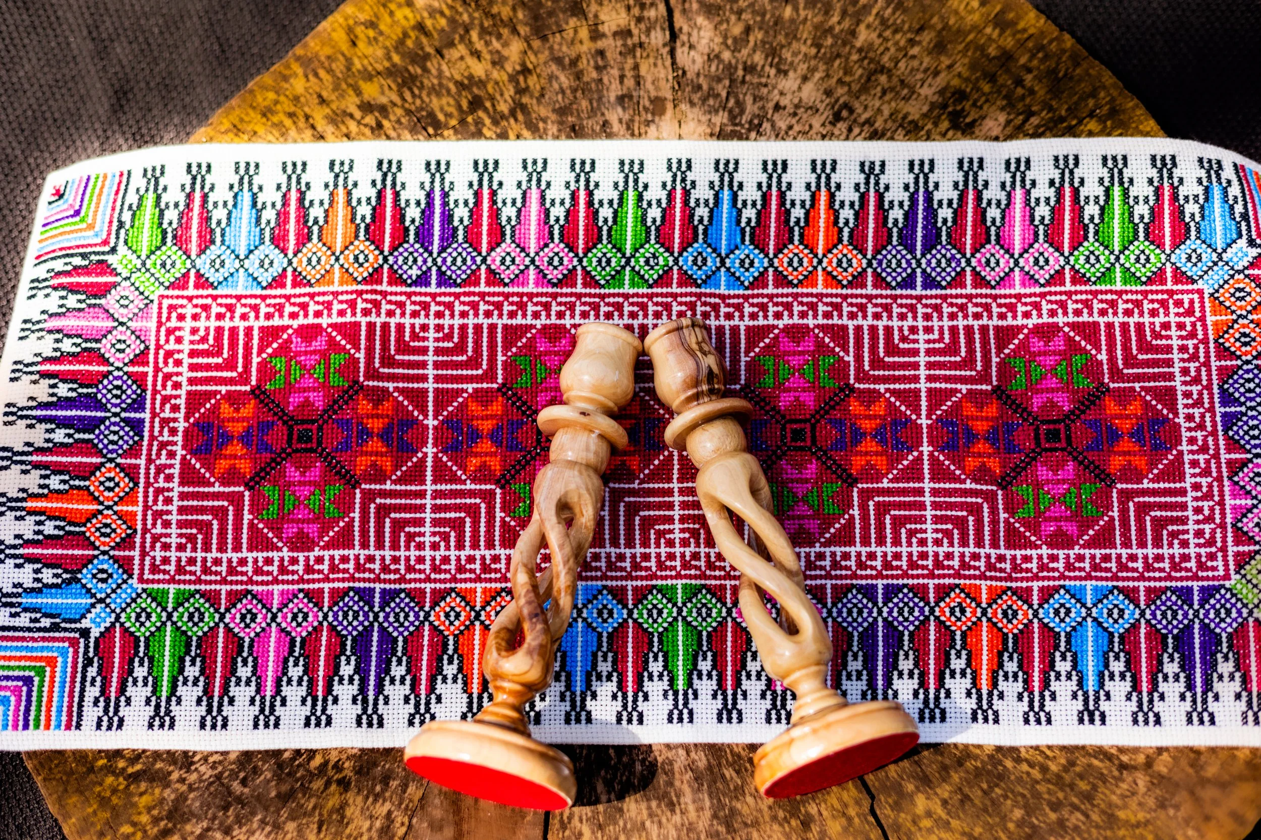 Close-up of colorful embroidered textile with wooden carved figurines on top, on a wooden surface.