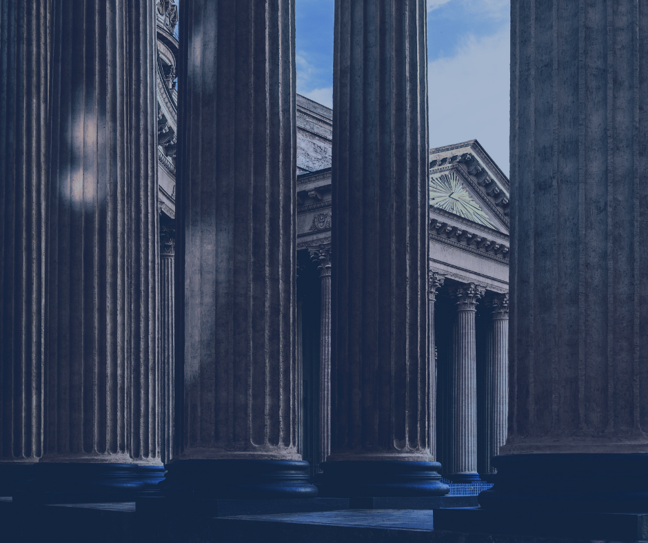 Photo of ancient Greek or Roman-style marble columns of a classical building or temple, with a blue sky in the background.