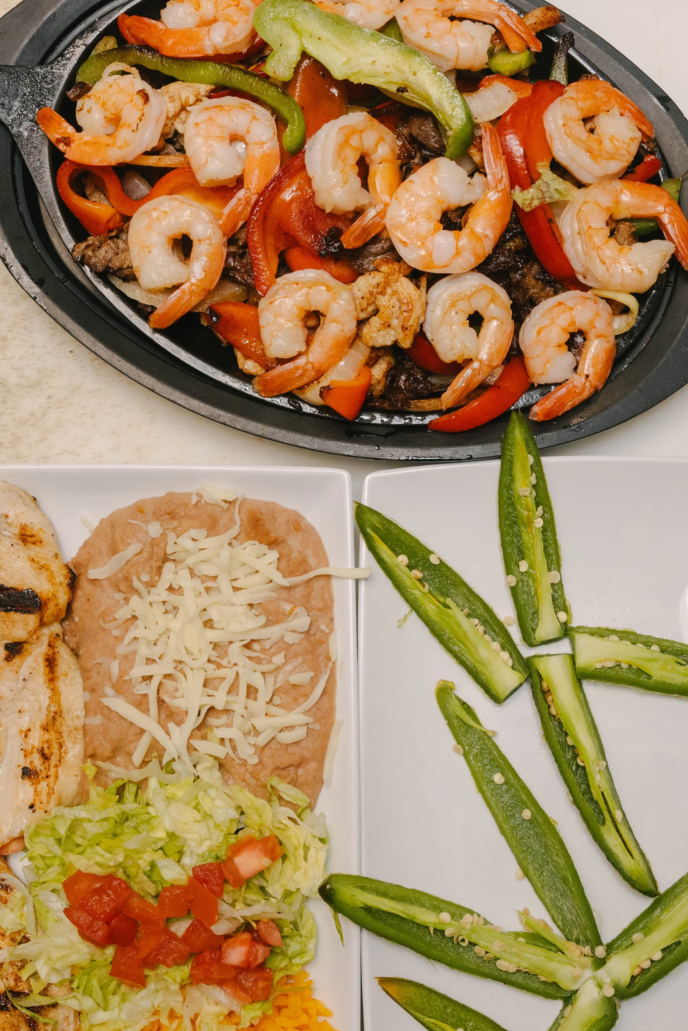 A plate of cooked shrimp and sautéed bell peppers, grilled chicken breast with shredded cheese, and fresh vegetable salads with lettuce, tomatoes, and cucumbers.