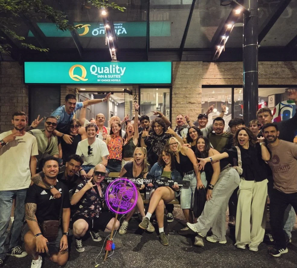 A full West Coast Party Crawl group posing with WCPC signs on Granville Street in Vancouver.