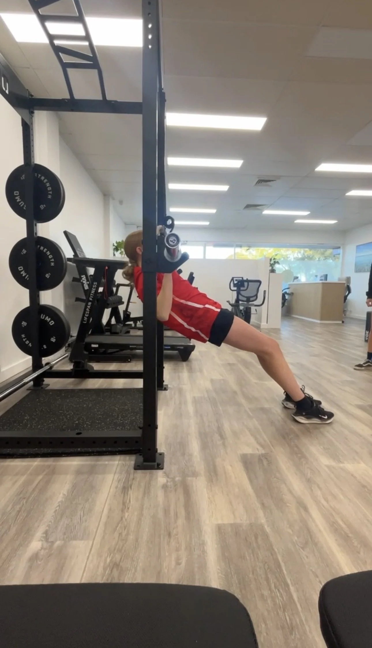 Person performing an inverted row exercise on a gym rack in a fitness studio
