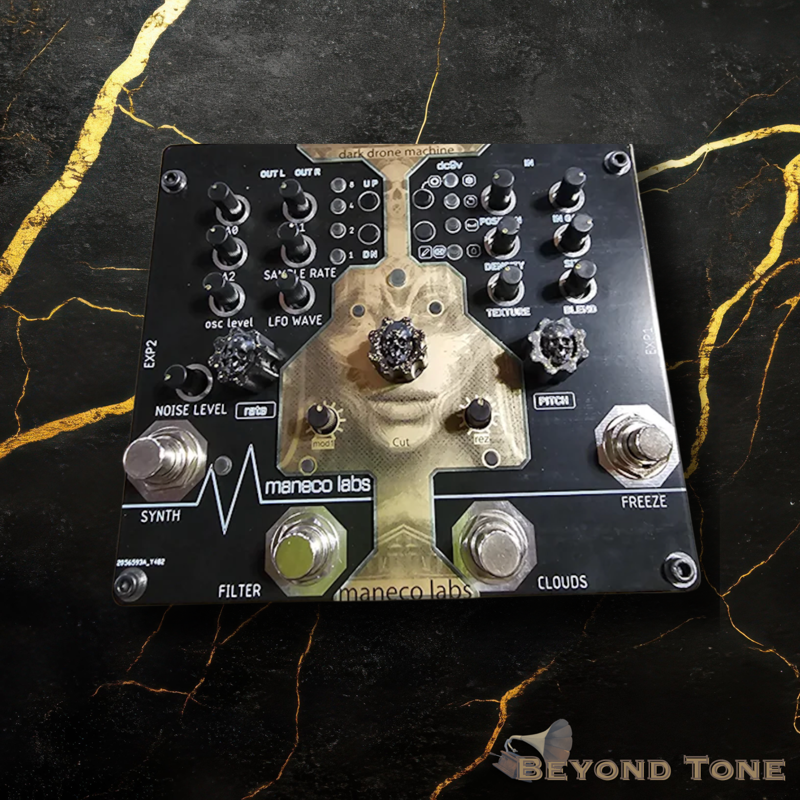 A black modular synthesizer with various knobs and switches, featuring artwork of a woman's face in the center, placed on a black marble surface with gold veining.