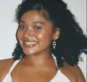 Portrait of a young woman with curly hair smiling, wearing earrings and a white top