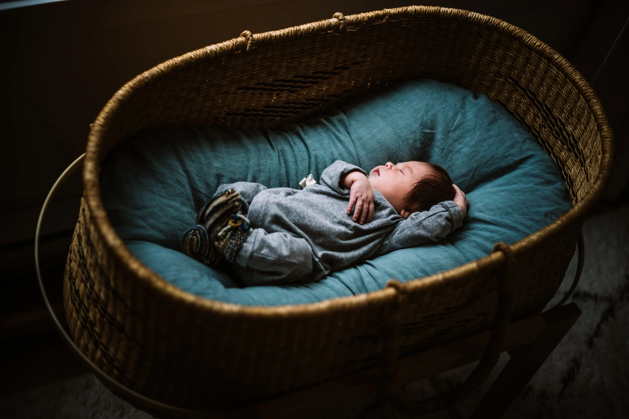 Baby sleeping in a wicker bassinet with blue bedding.