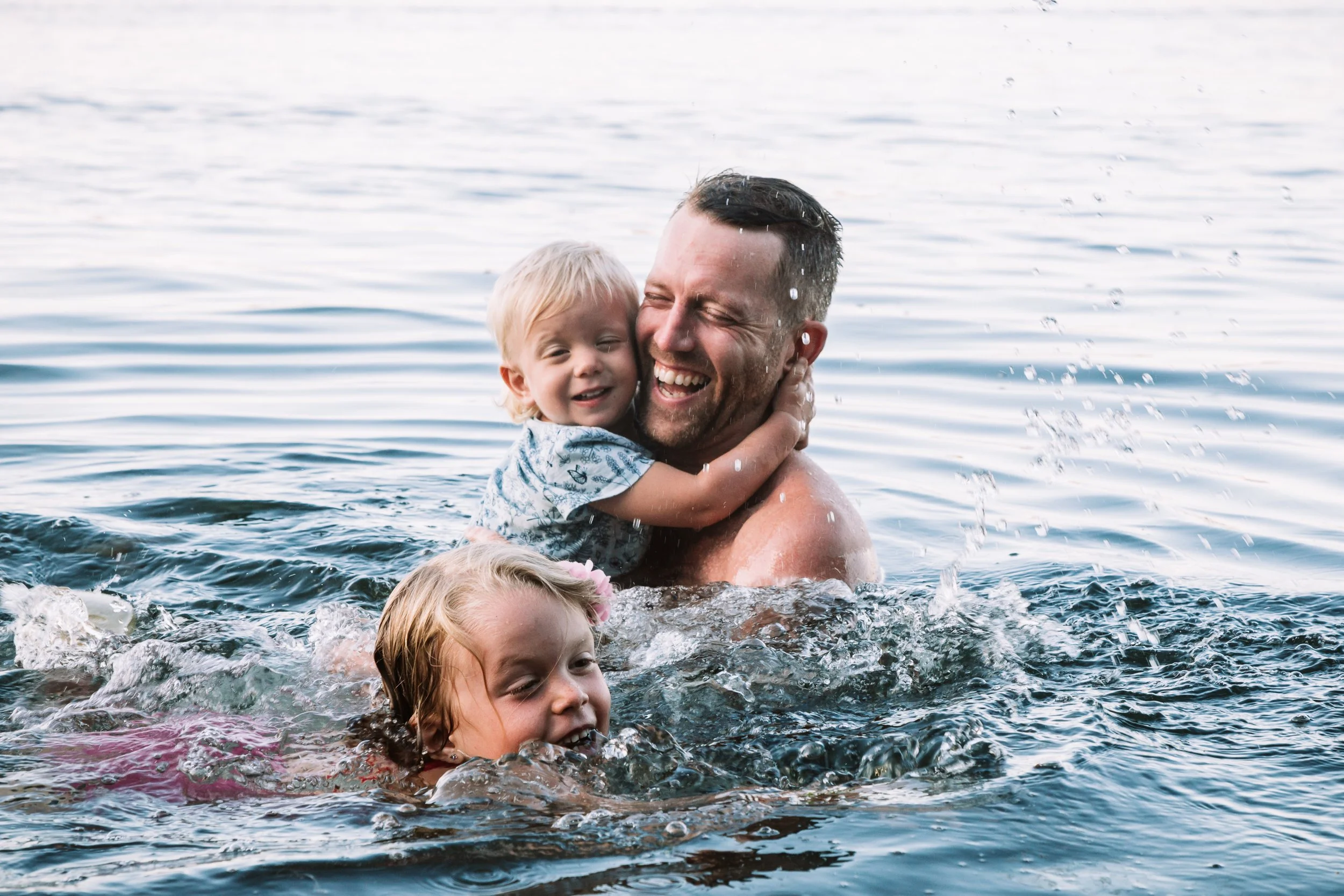 Family playing in the water, man with two children.