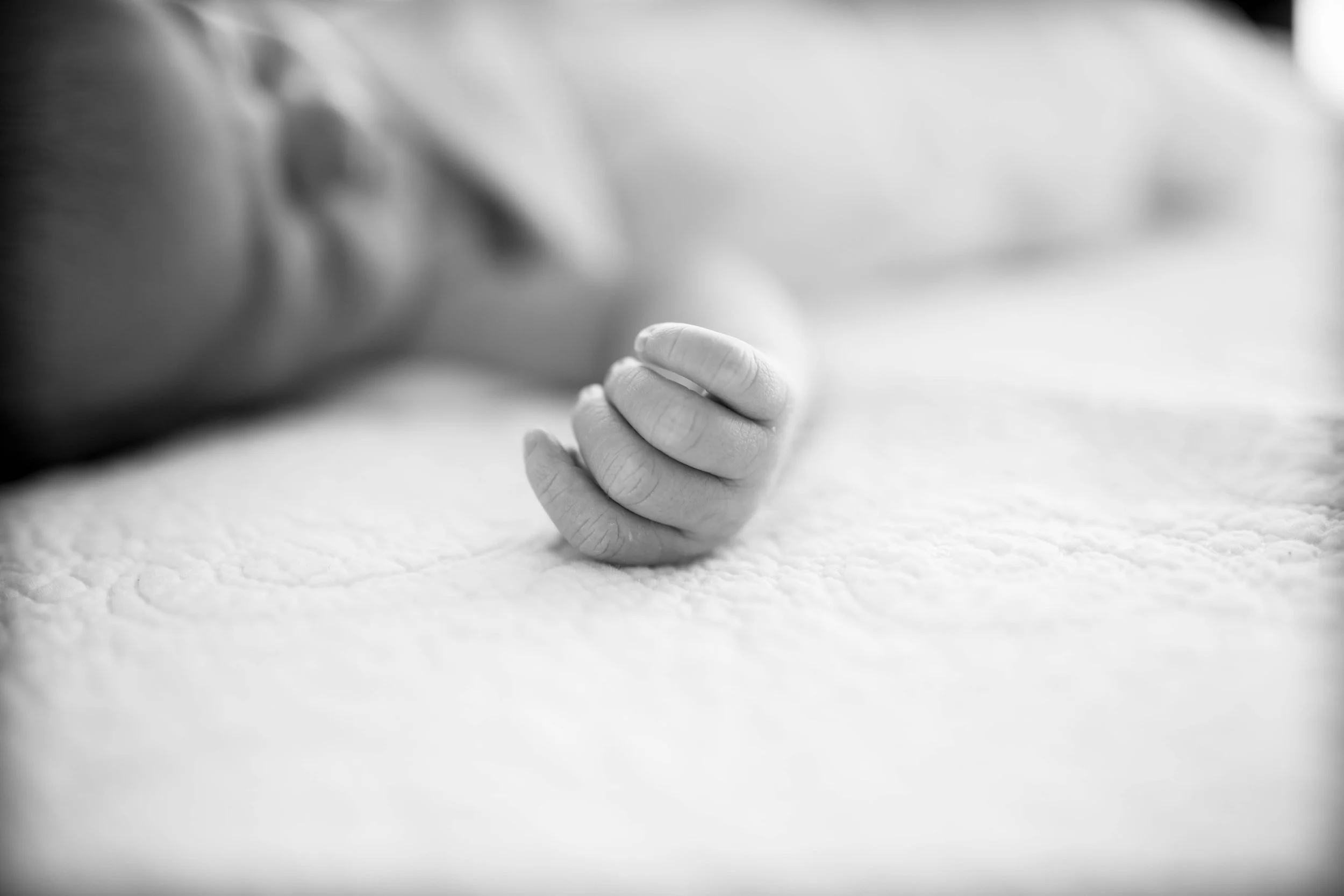 Black and white photo of a baby's hand resting on a textured surface.