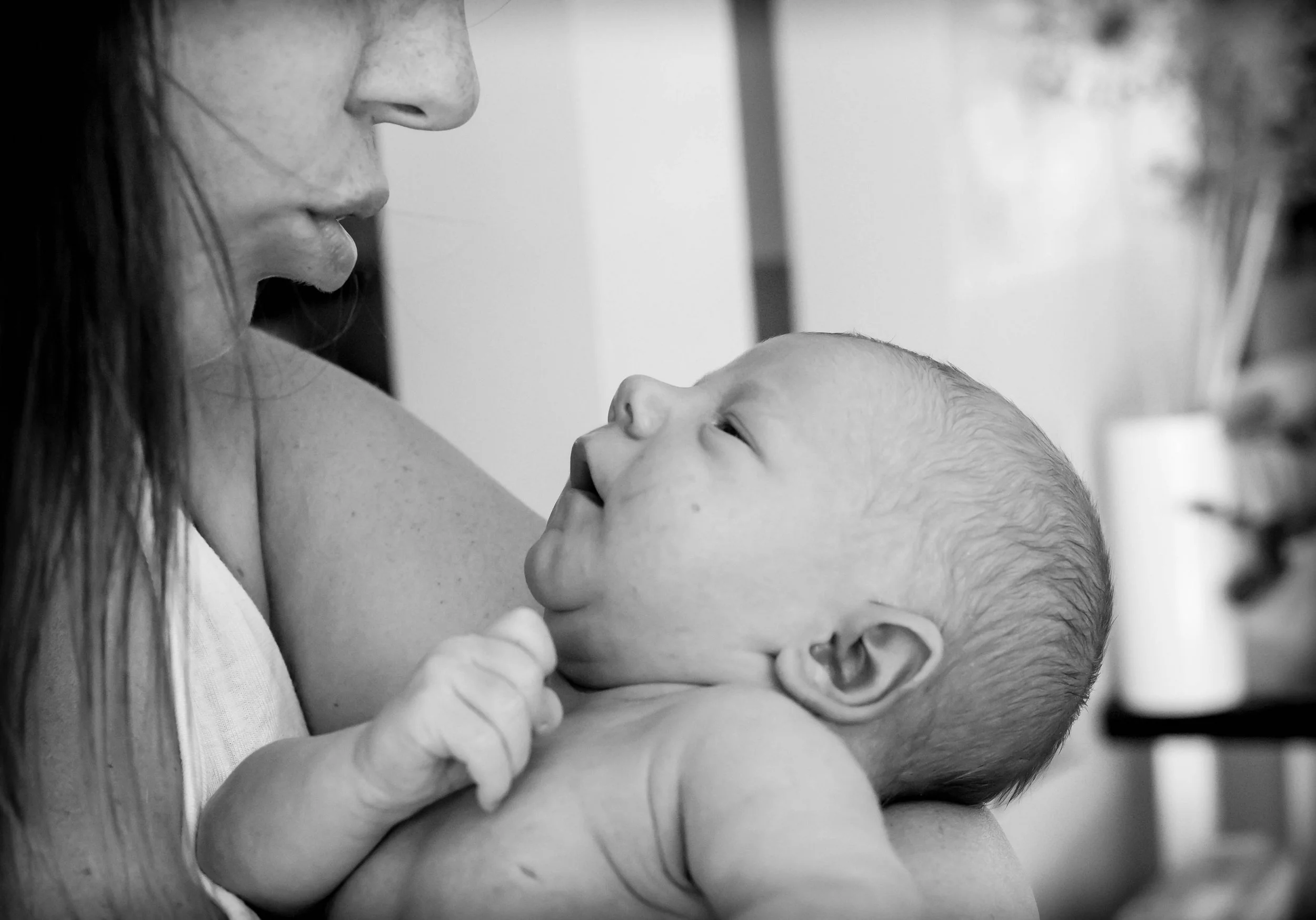 Black and white photo of a mother holding a newborn baby close to her face, looking at each other.