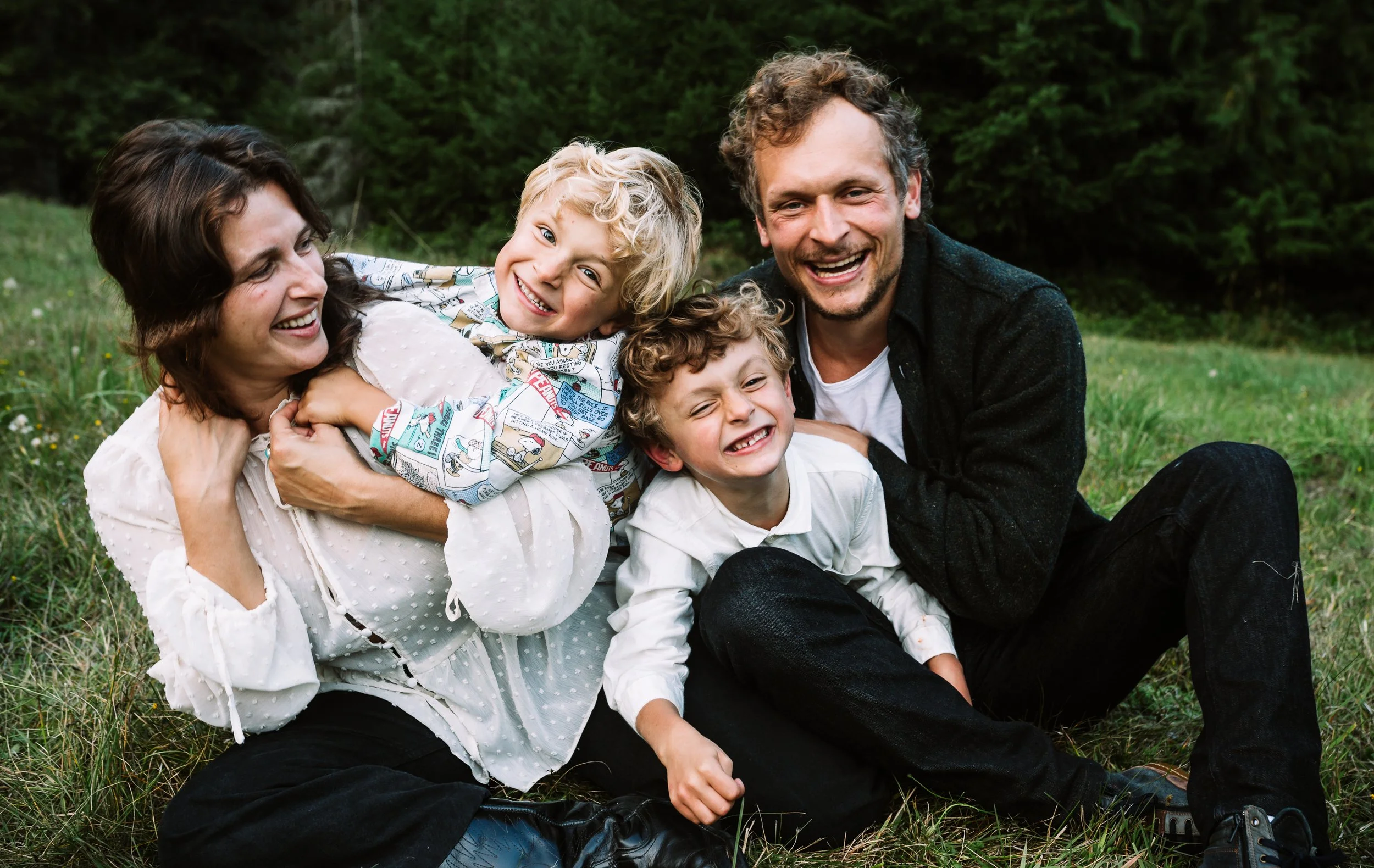 Family sitting together on grass, smiling and embracing outdoors.