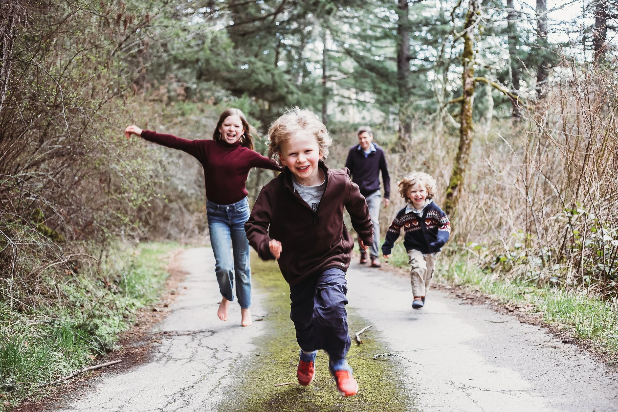 Children running joyfully on a forest path with trees in the background.