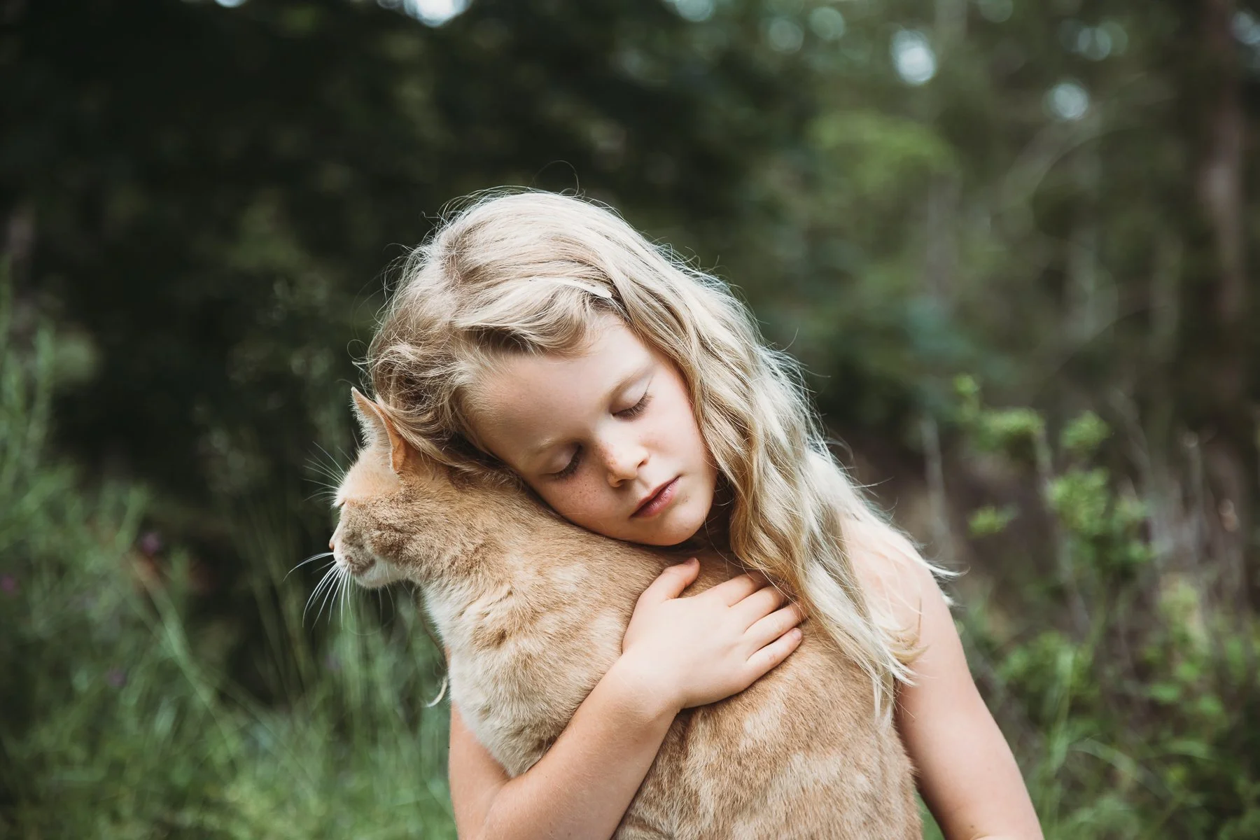 Child affectionately hugging an orange tabby cat outdoors.