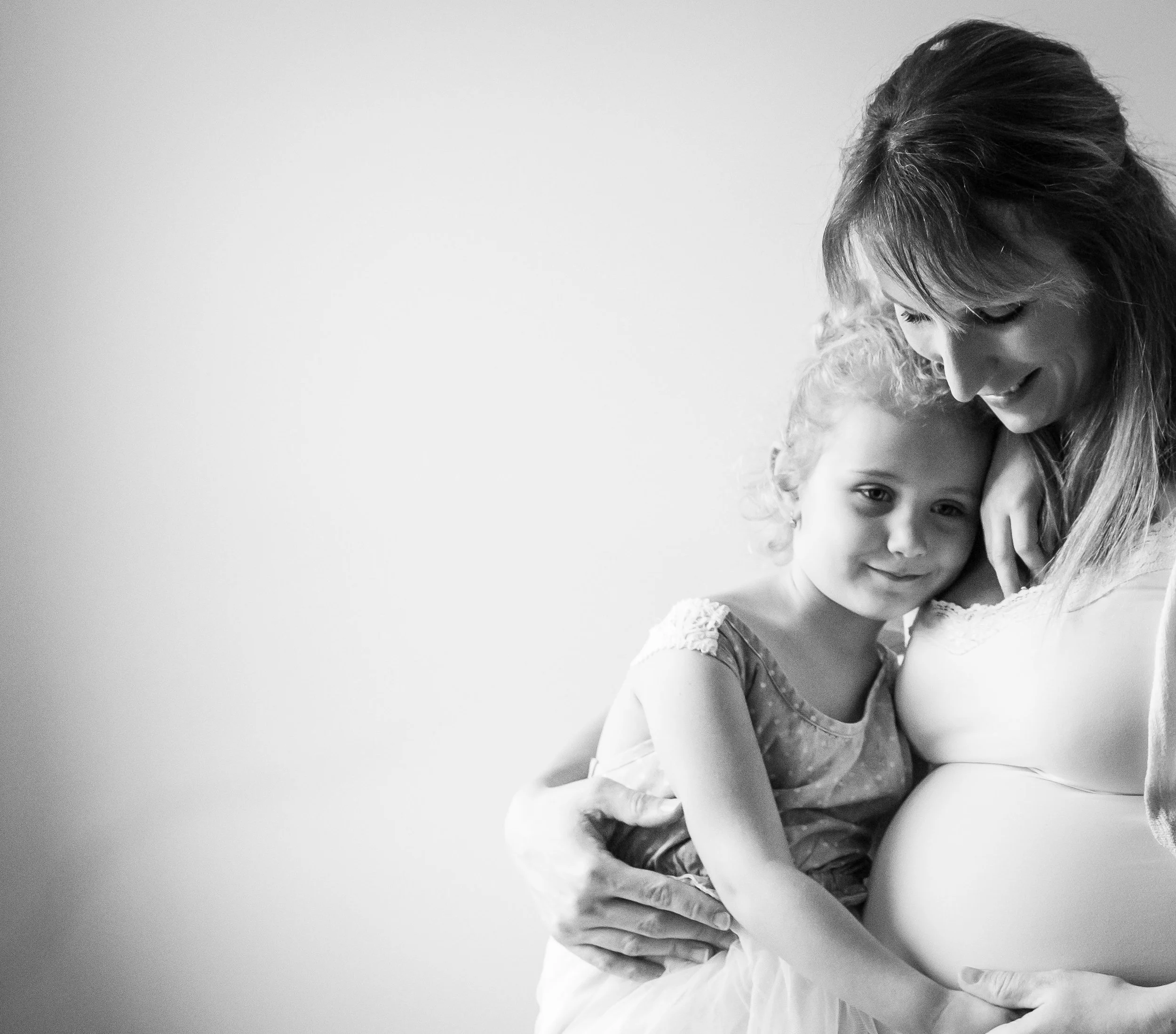 Pregnant woman hugging young girl, both smiling, black and white photo.