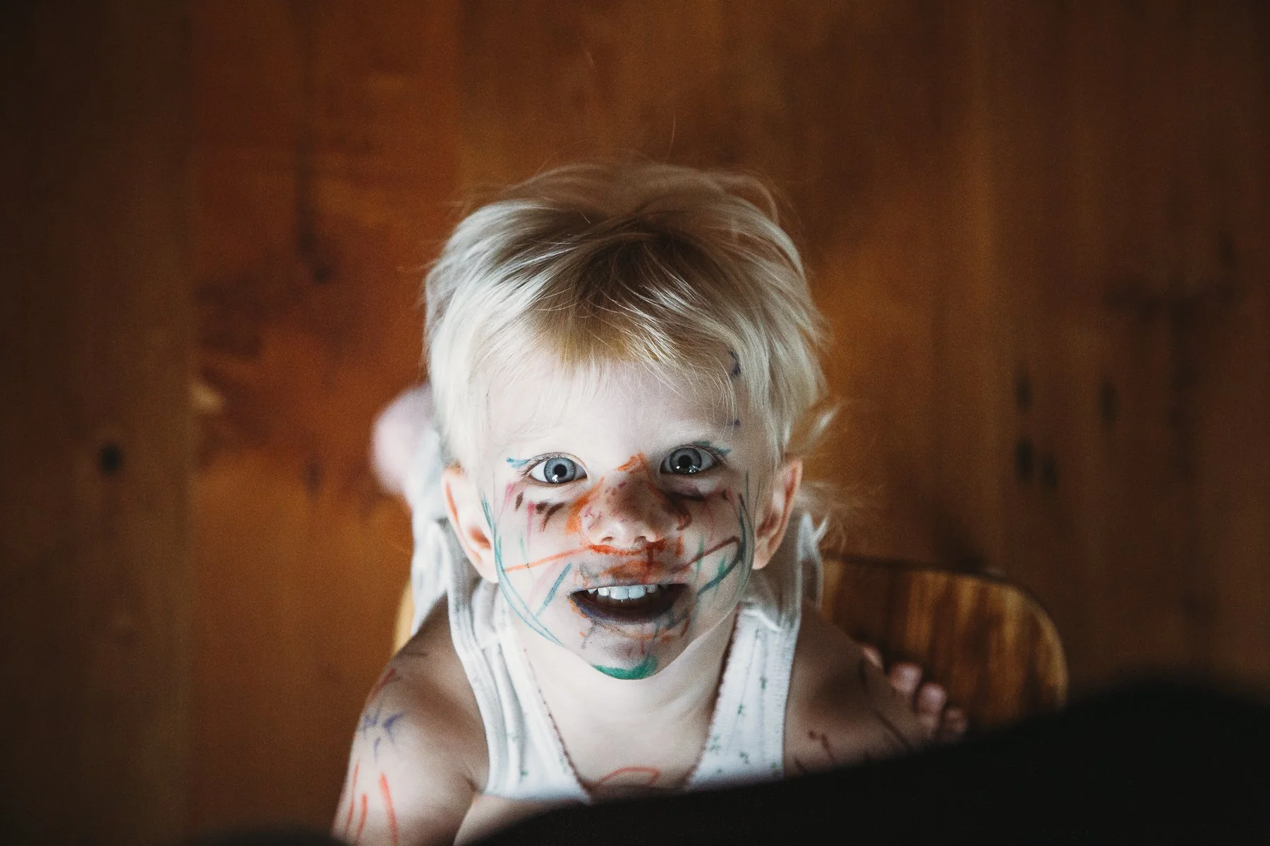 Happy child with face painted with colorful markers, smiling at the camera.