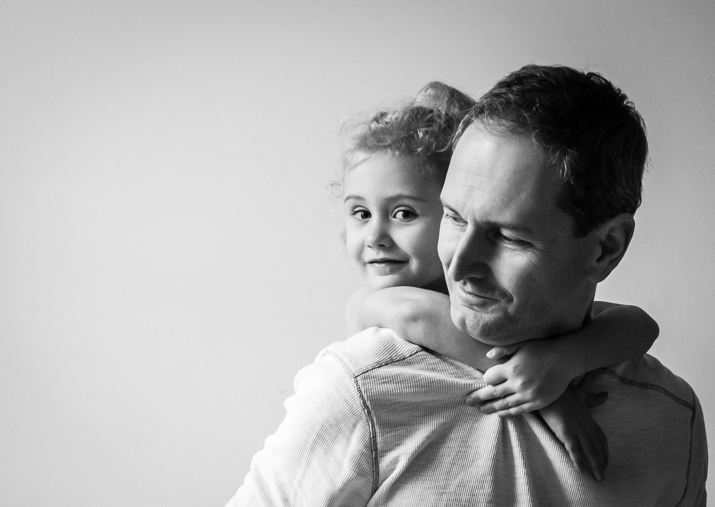 Black and white photo of a child hugging a man from behind, both smiling.