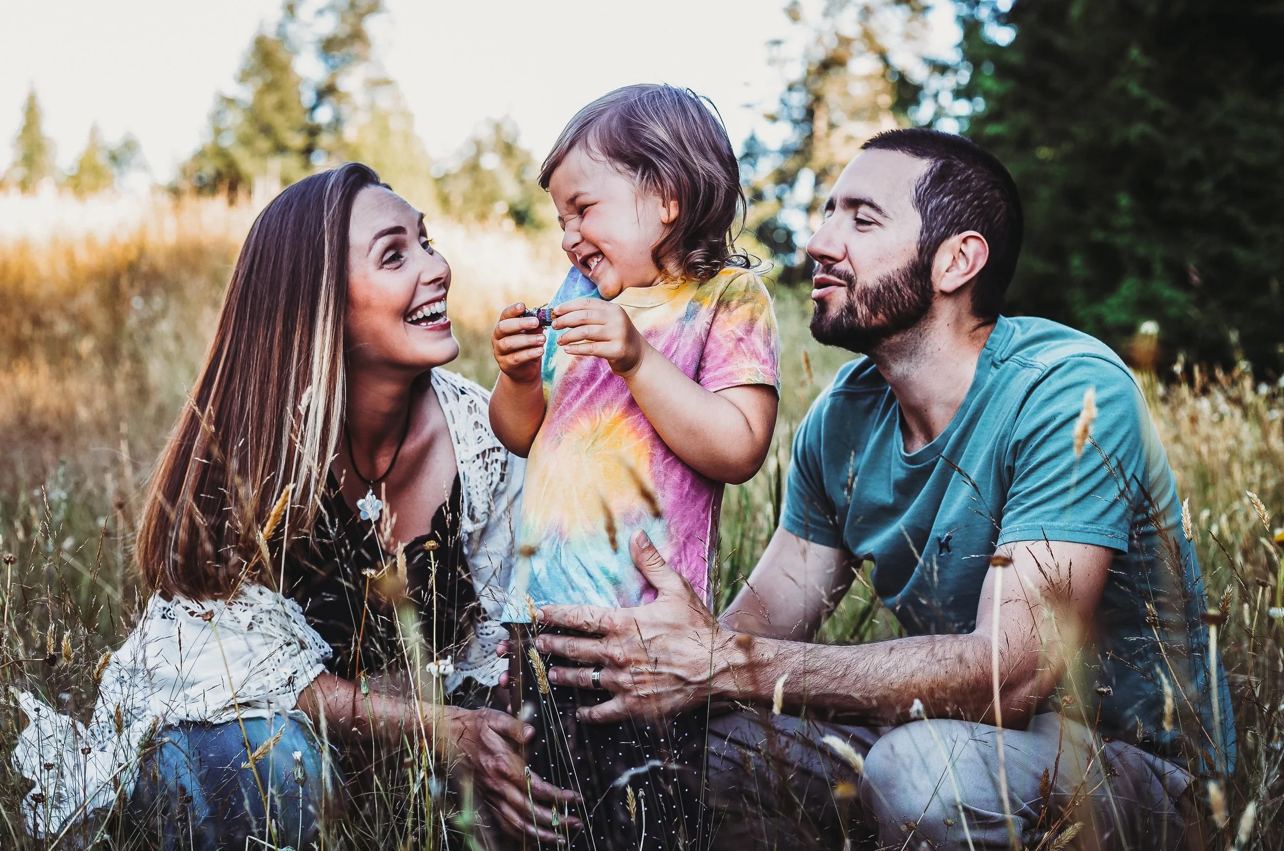 Family laughing in a field, kid holding flowers