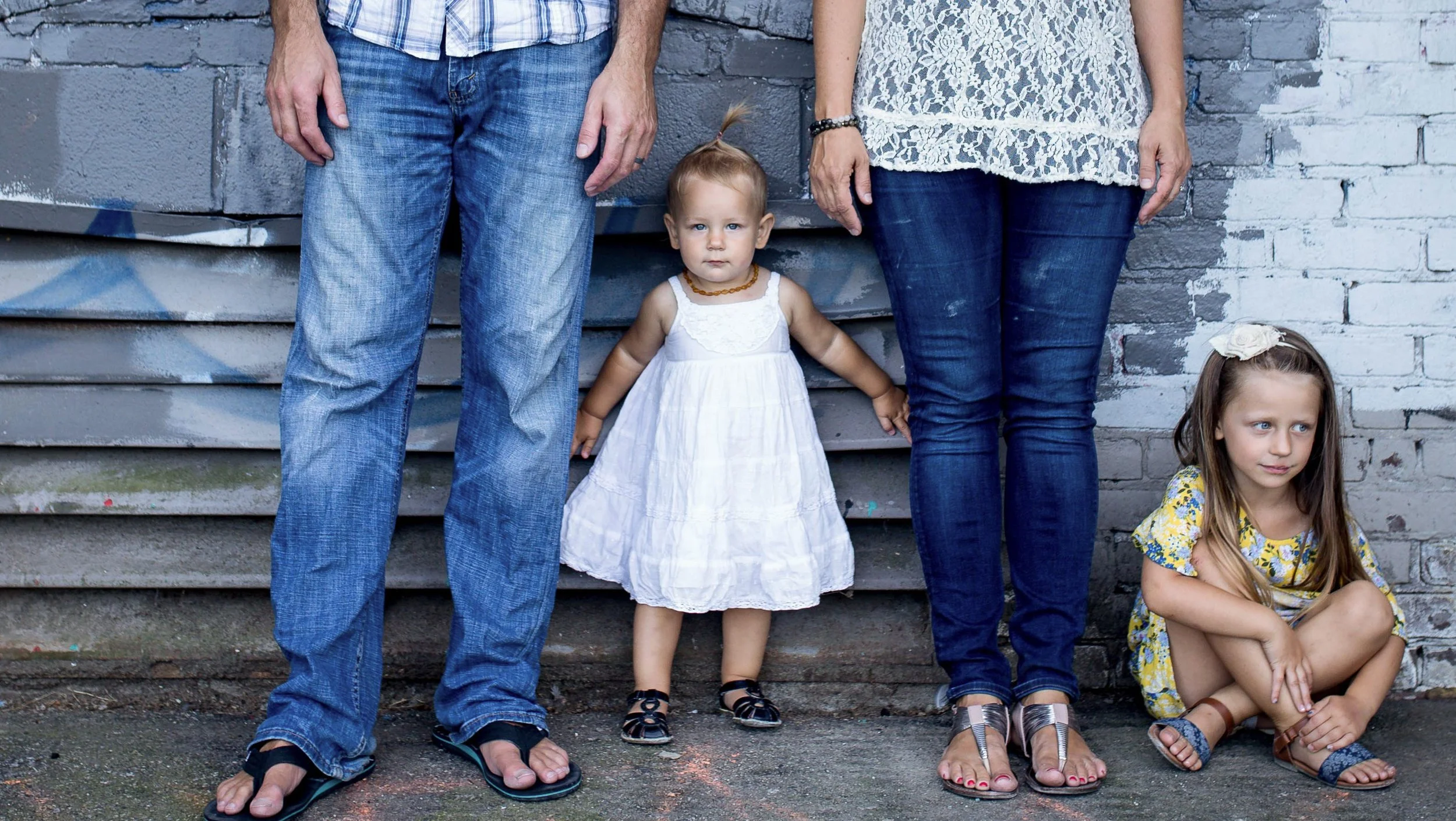 Family photo with toddler and young girl against urban wall.