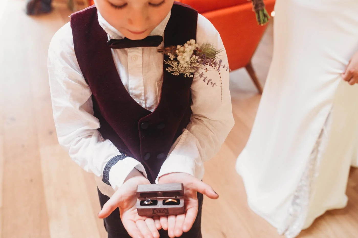 Child in formal attire holding a ring box with two rings at a wedding.