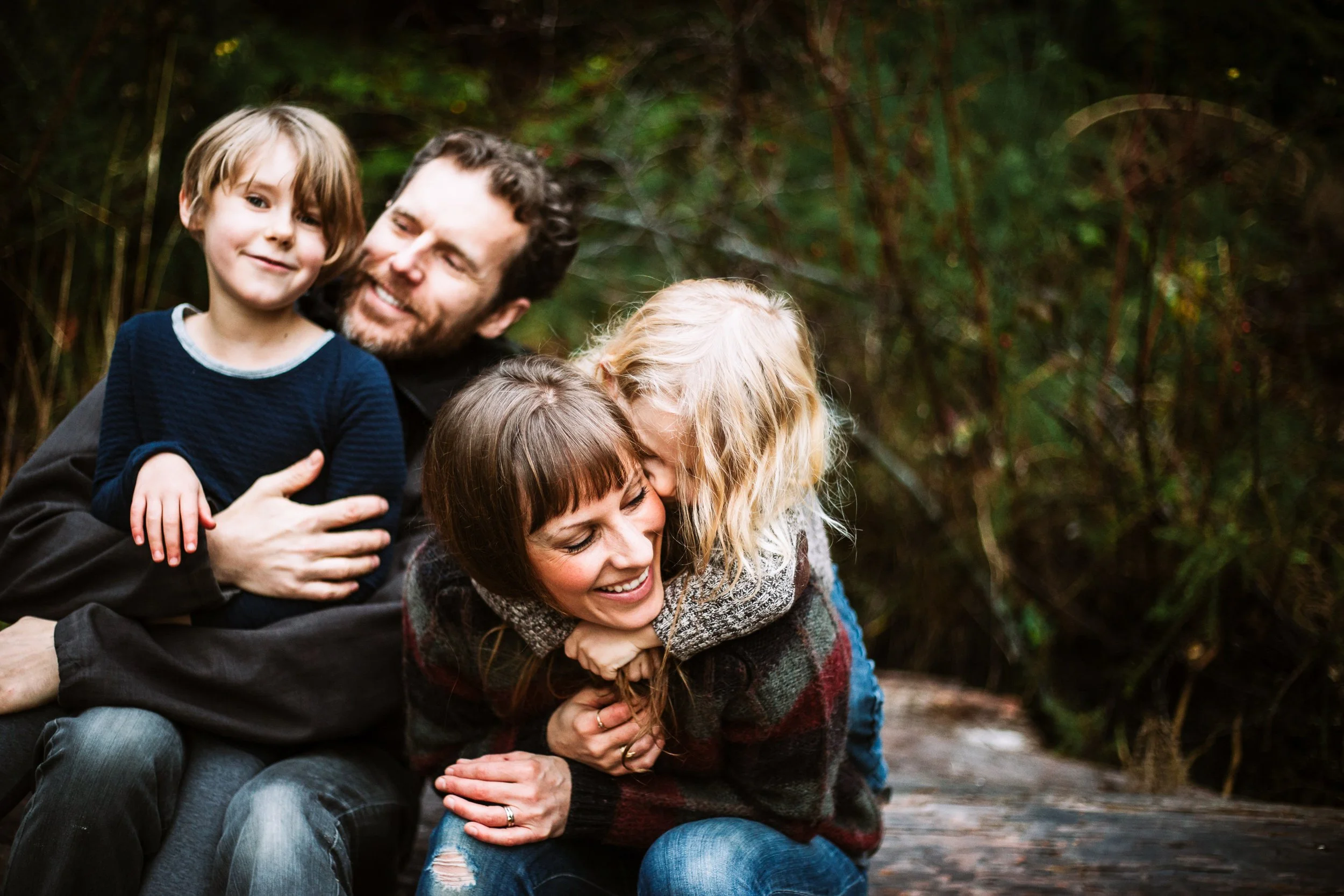 Family enjoying outdoor moment, with parents and two children smiling and embracing each other in a natural setting.