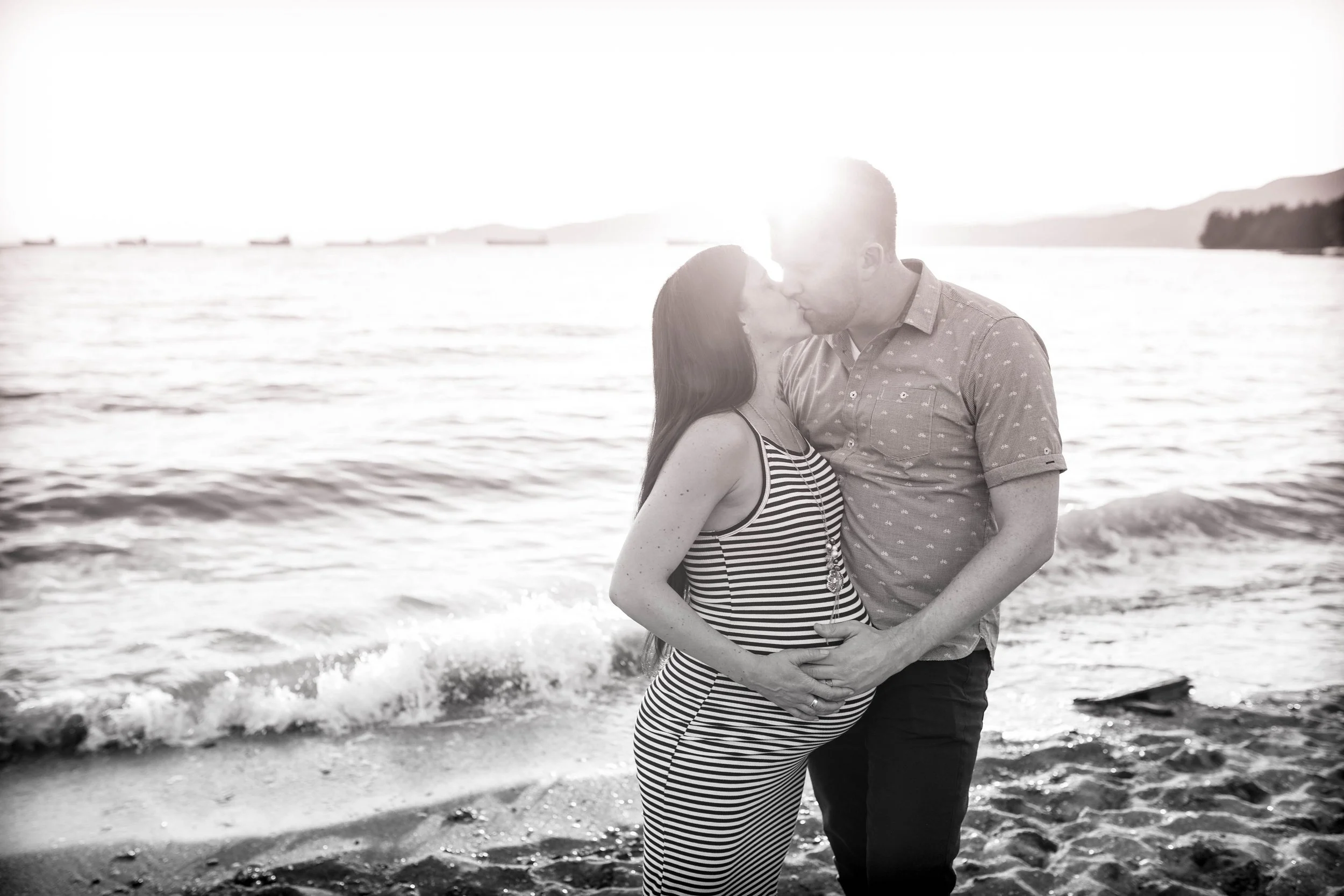 Pregnant couple kissing on the beach at sunset.
