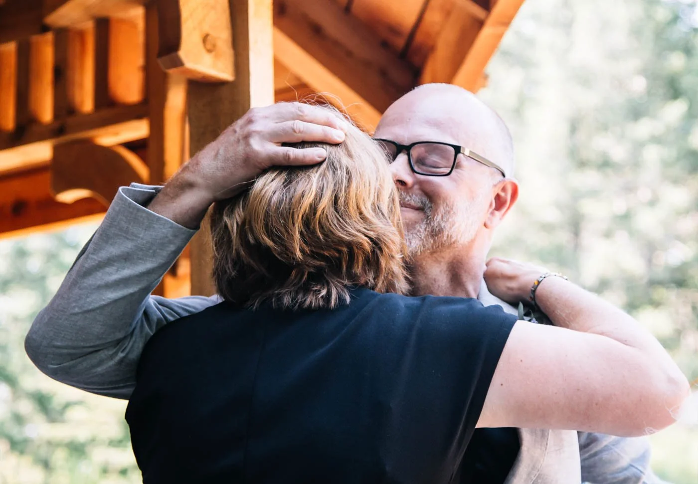 Two people hugging outdoors, surrounded by wooden structure.