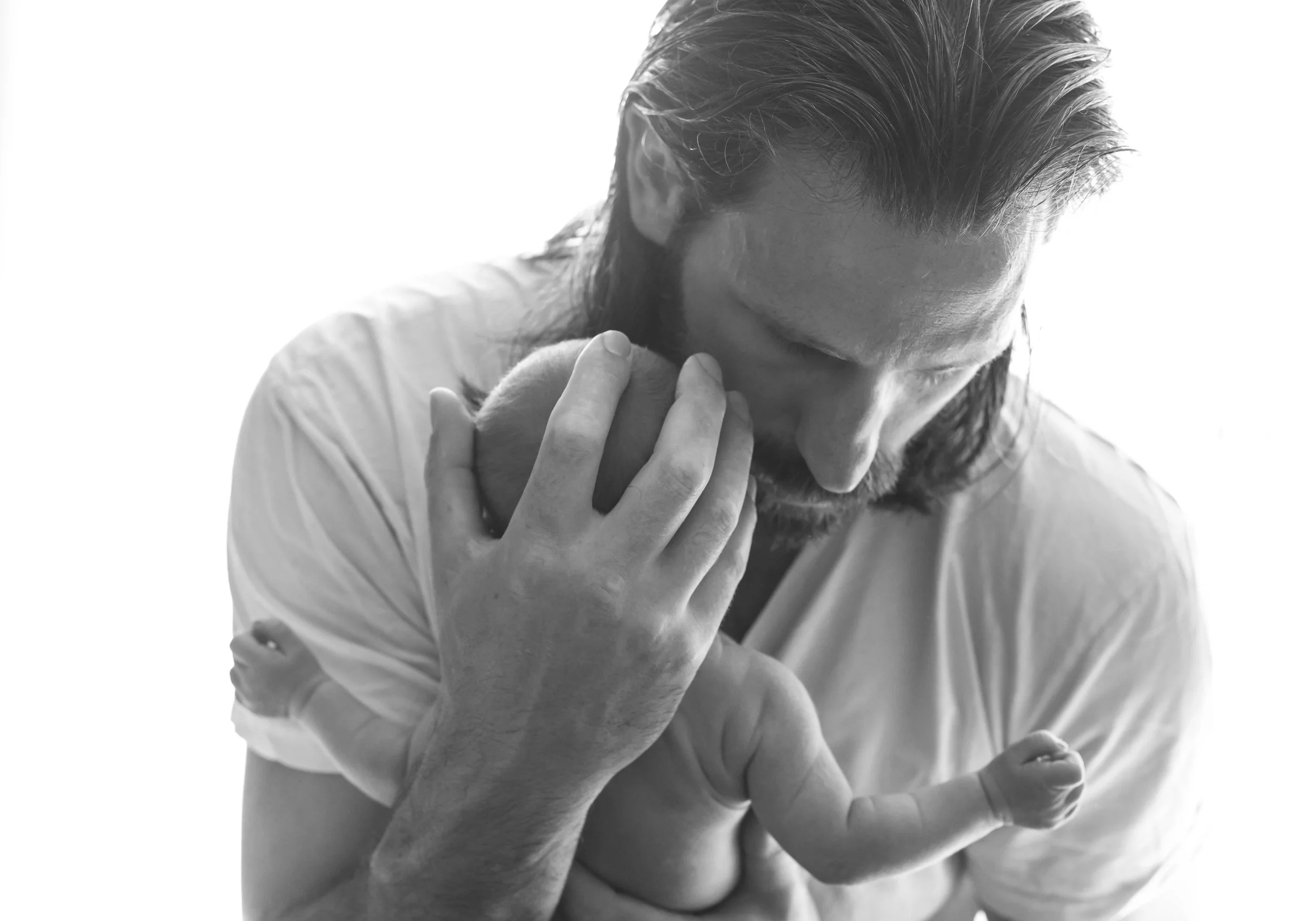 Black and white photo of a man tenderly holding a newborn baby, capturing an intimate bonding moment.