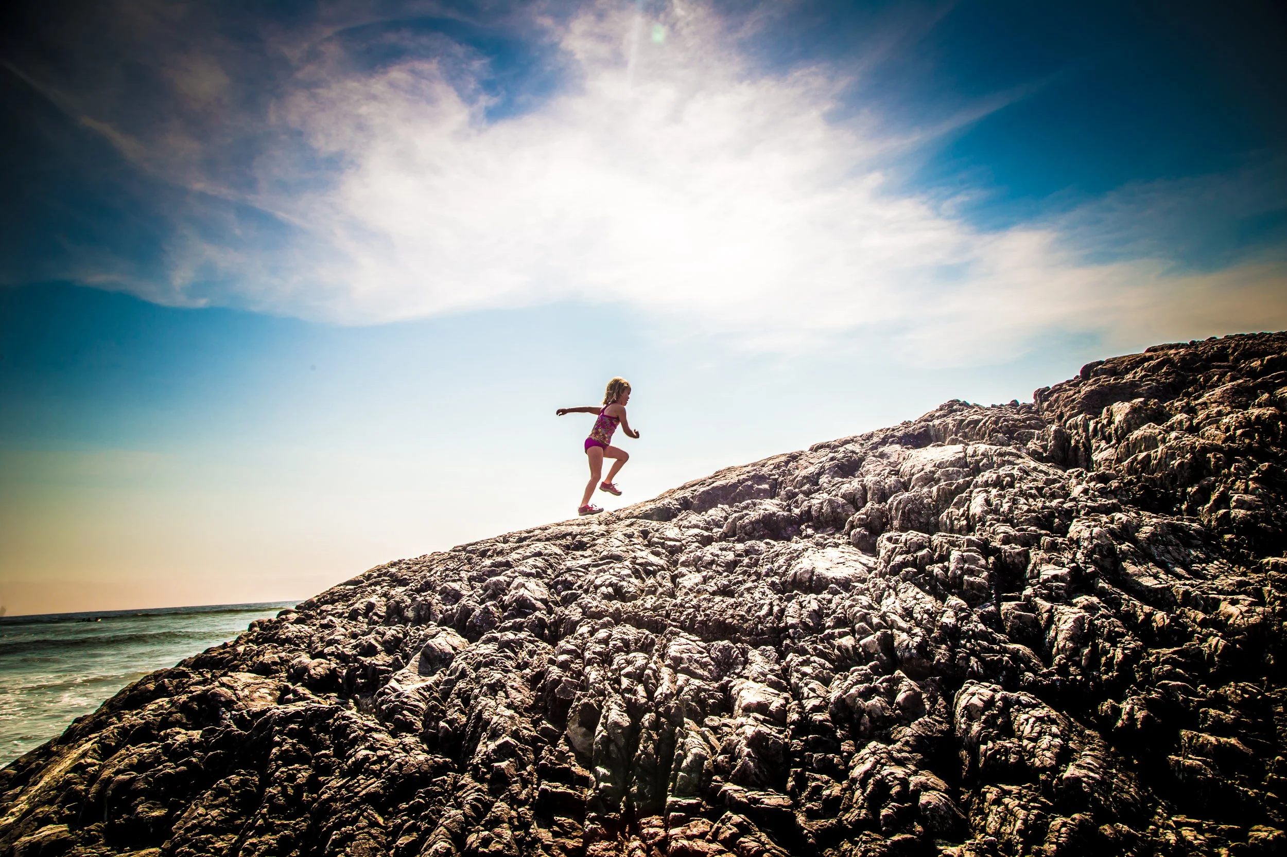 Child running on rocky hill by the sea under a blue sky.