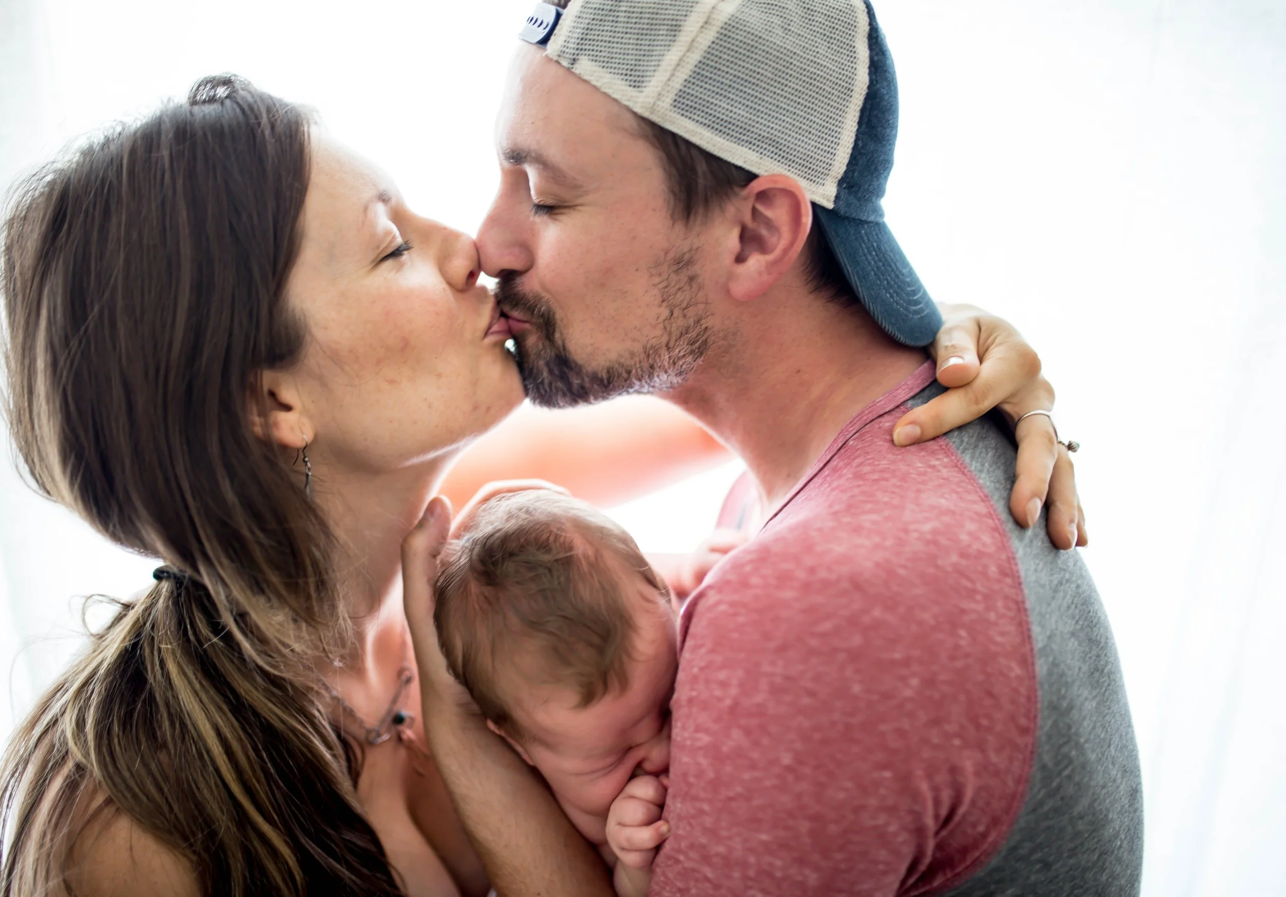 Couple kissing while holding a newborn baby