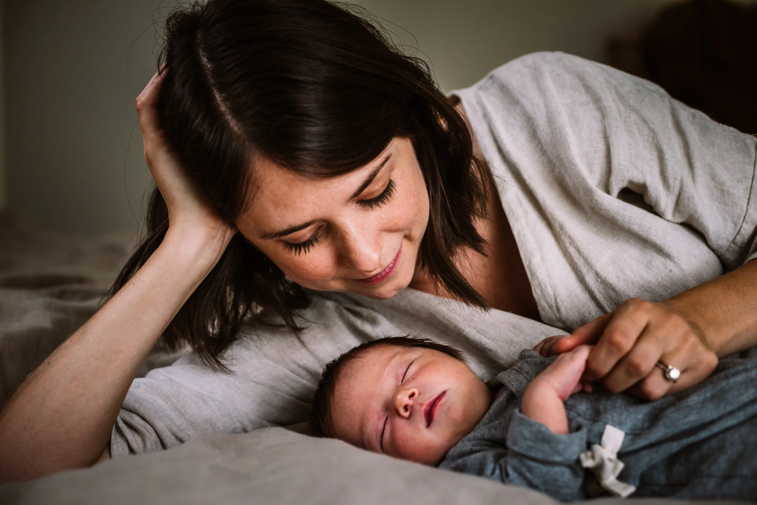 Mother lying beside sleeping baby, tender moment.