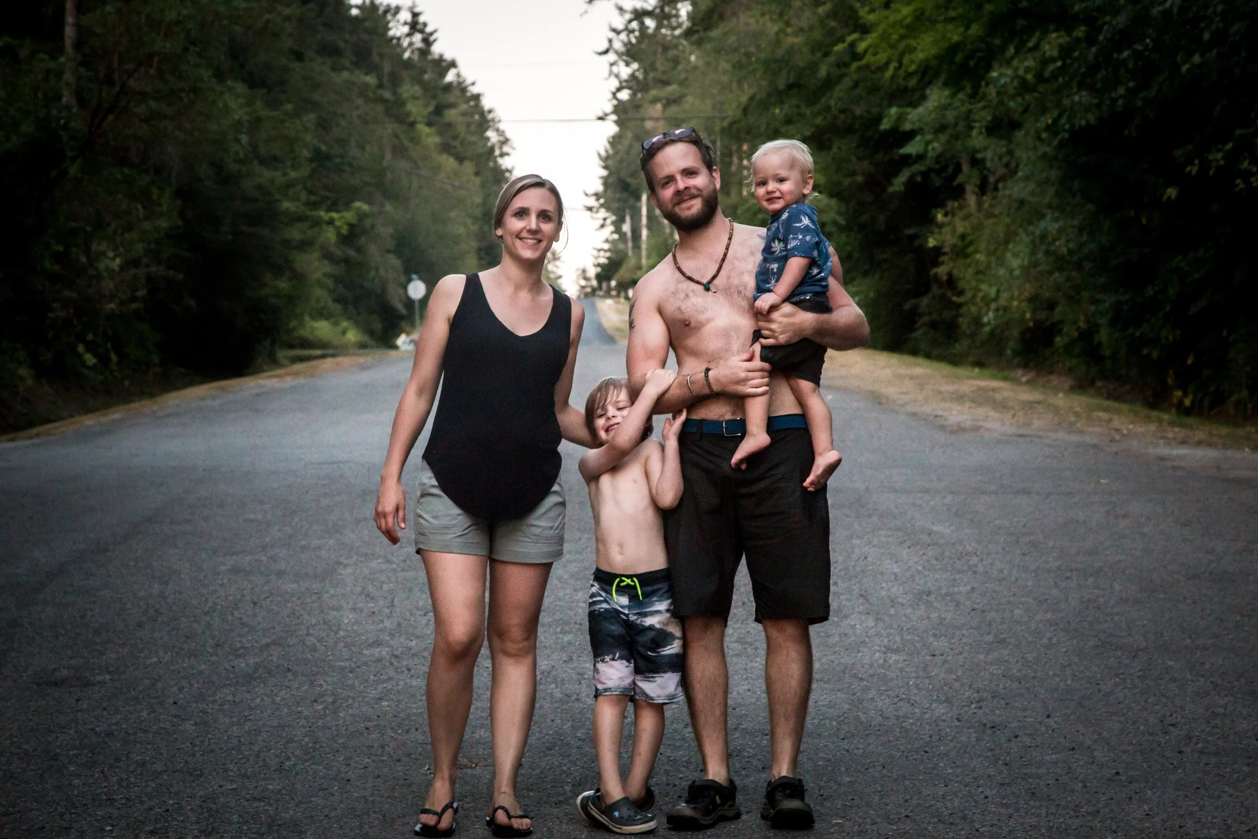 Family walking on a rural road, surrounded by trees.