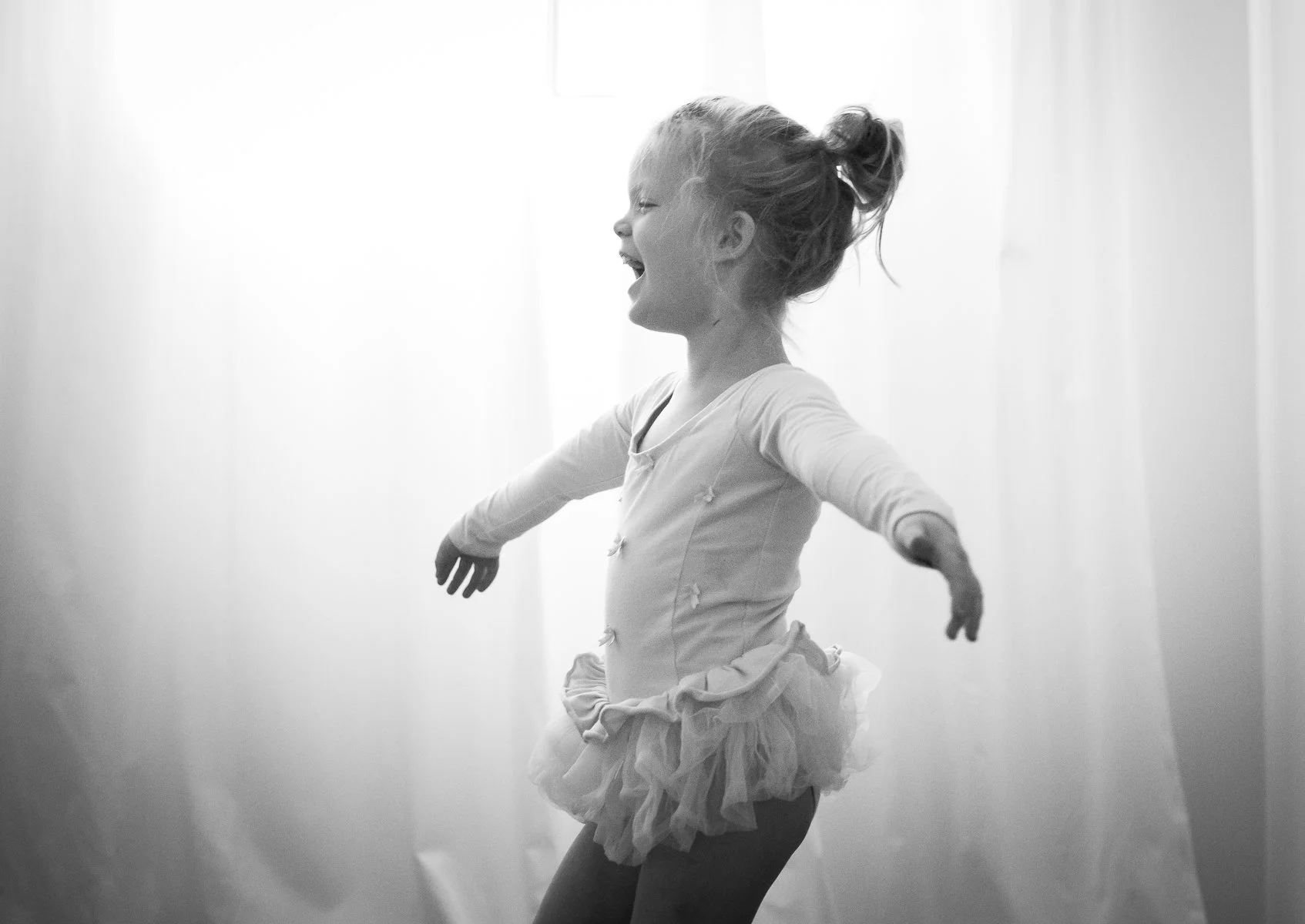 Black and white image of young girl in ballet dress dancing and smiling.