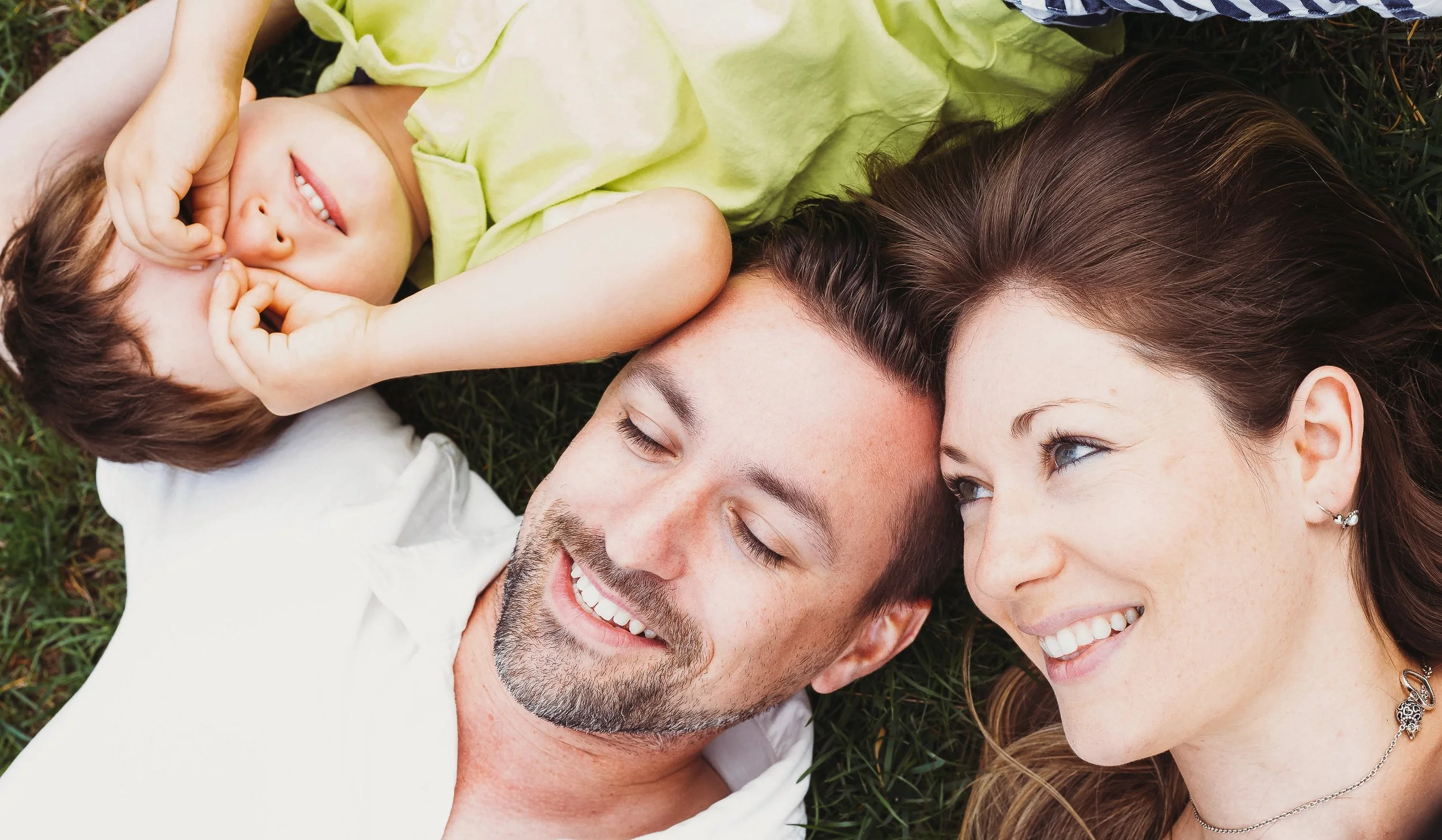 Happy family lying on grass, smiling and enjoying time together.