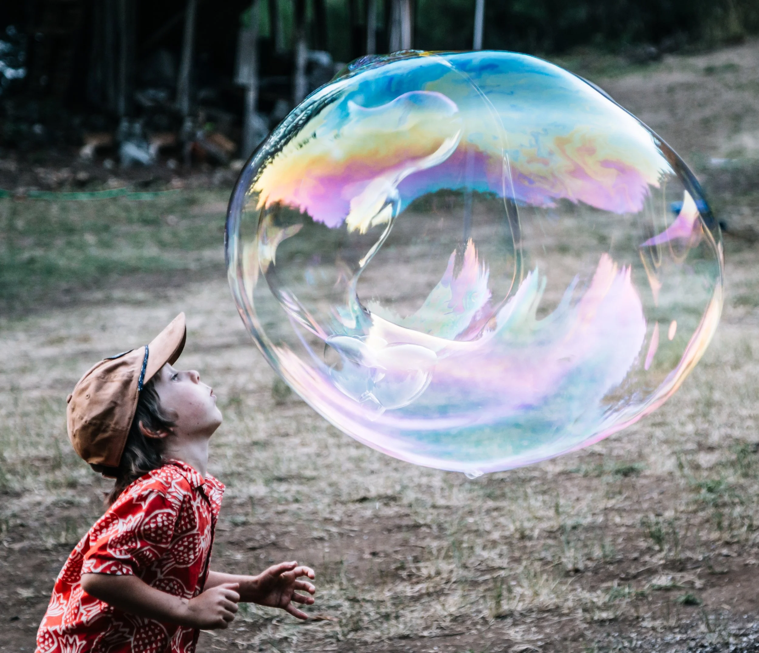 Child in red shirt playing with a large colorful soap bubble in a yard.