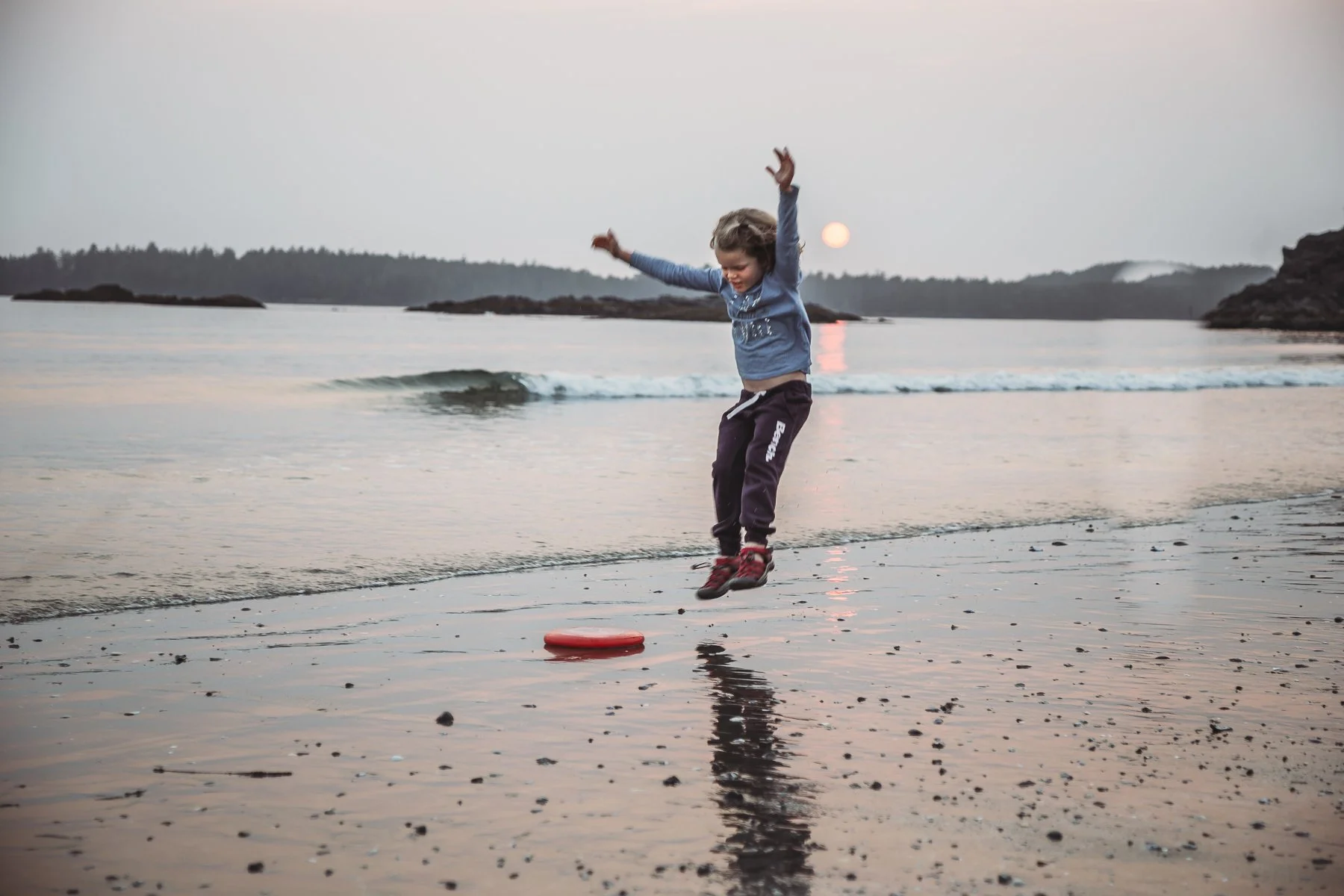 Child jumping over a frisbee on a beach at sunset