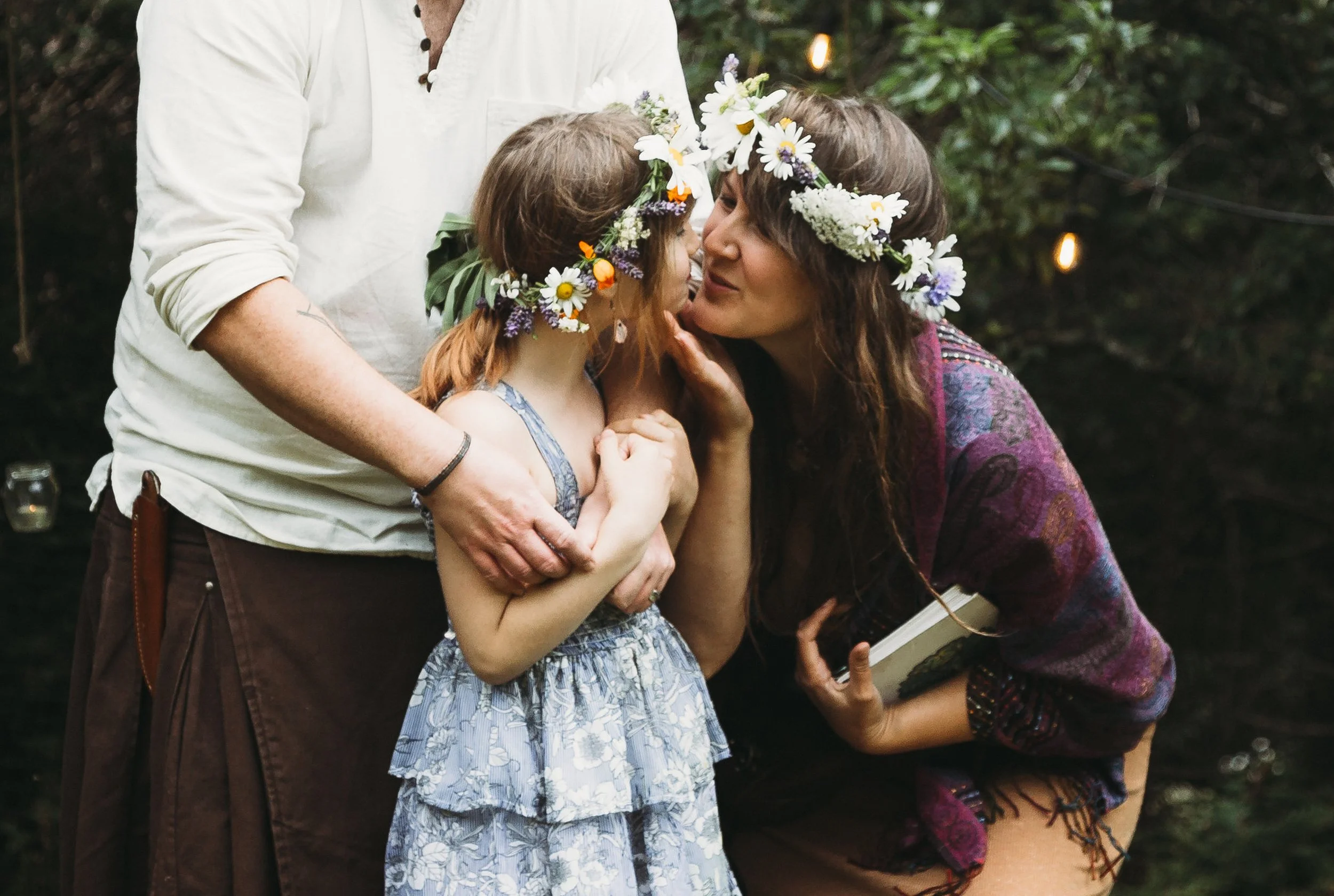 Woman in flower crown kissing child with flower crown outdoors