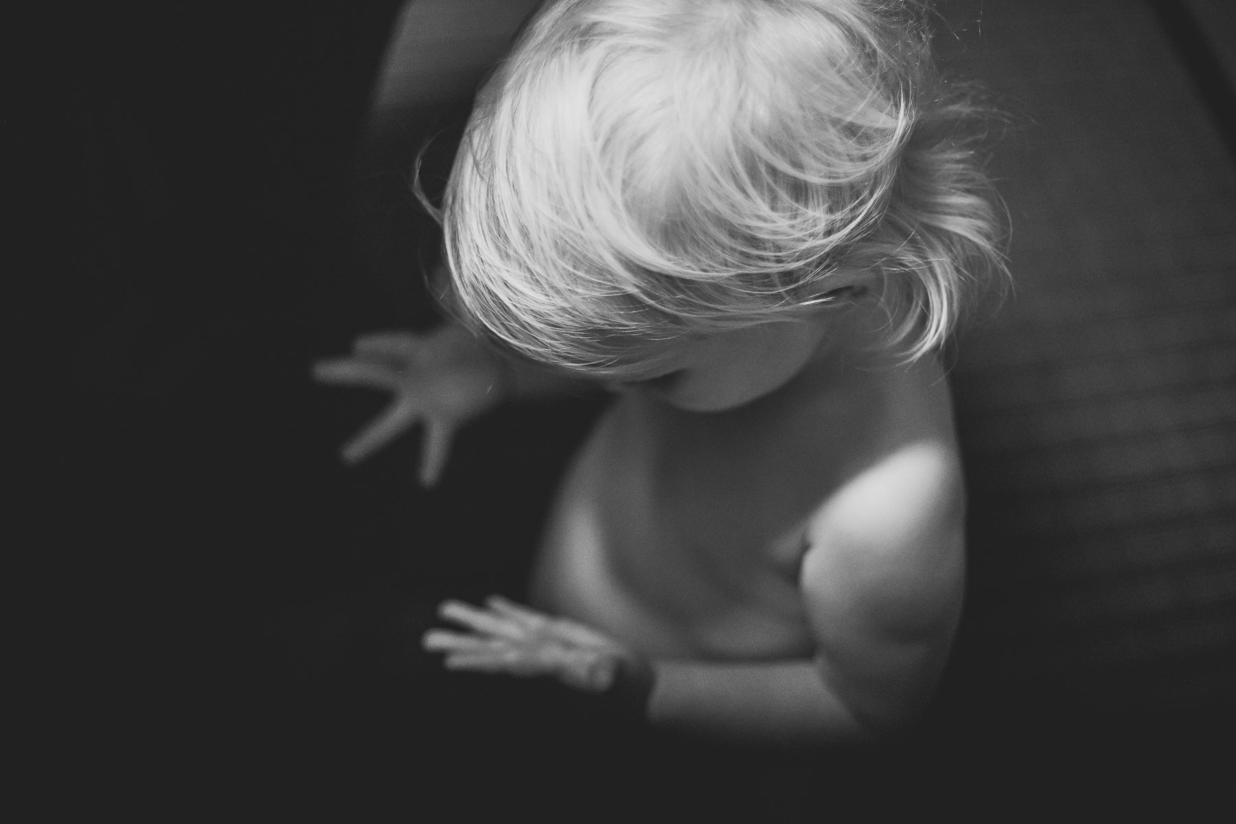 Black and white photo of a young child with light-colored hair looking down, shot from above.