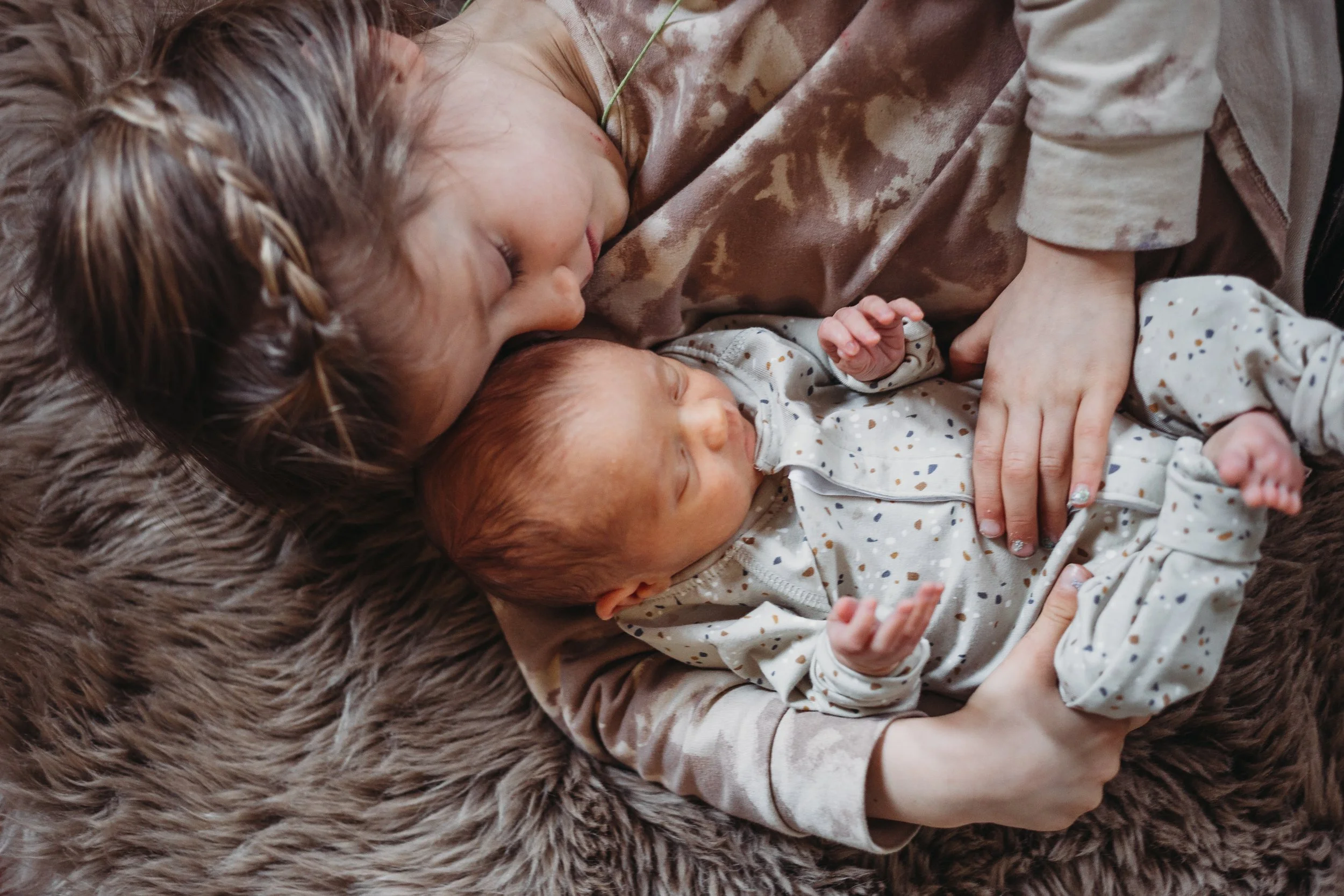 Child cuddling a newborn baby on a soft fur blanket.