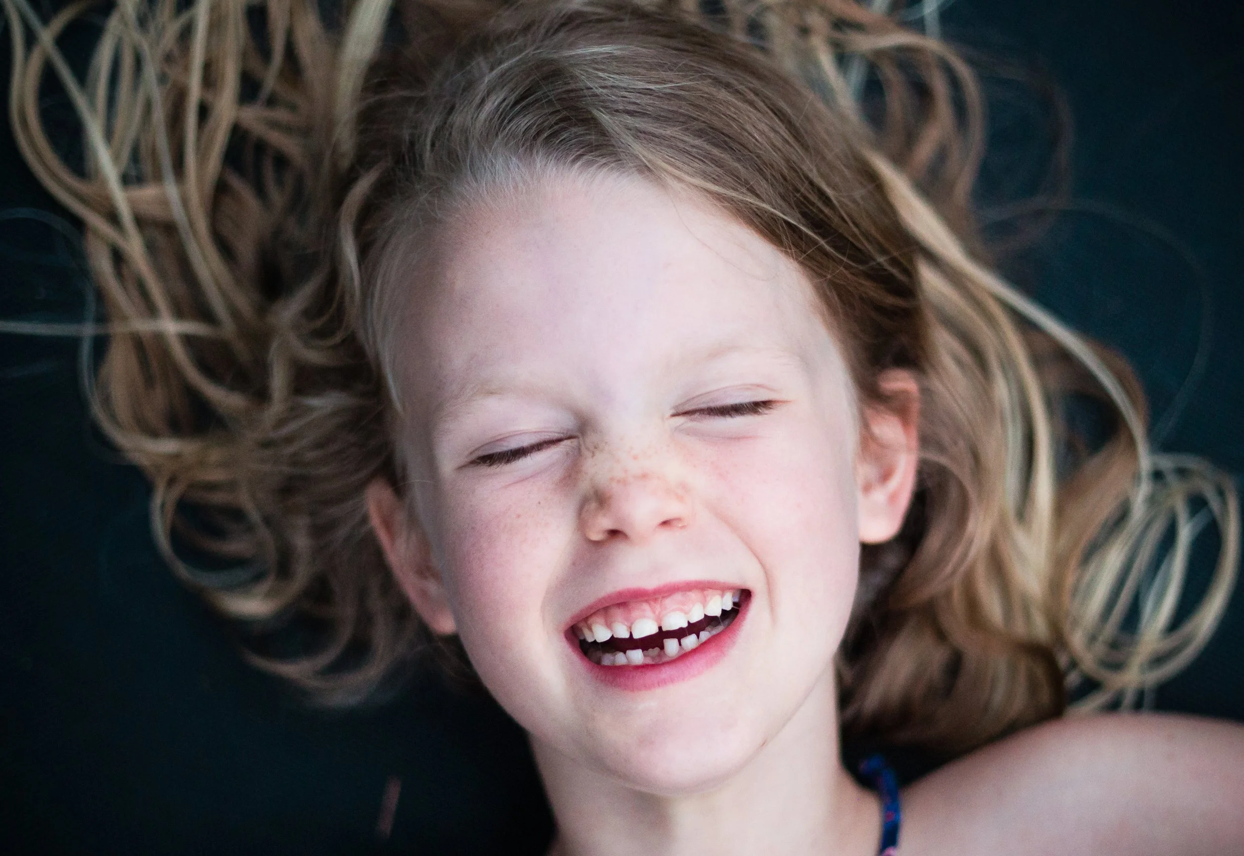 Close-up of a smiling child with closed eyes and blonde hair spread out.