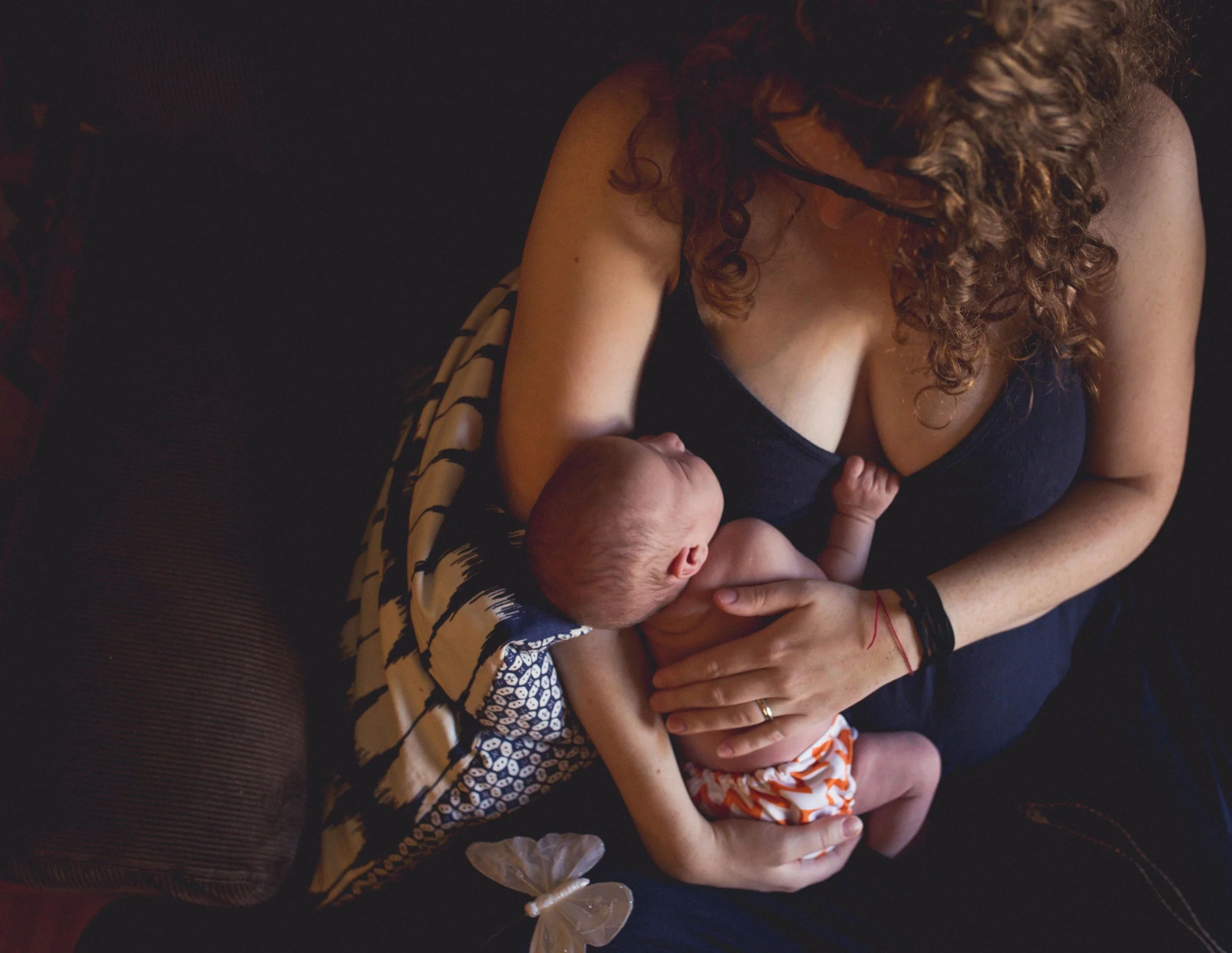 Mother breastfeeding newborn baby while seated on a sofa.