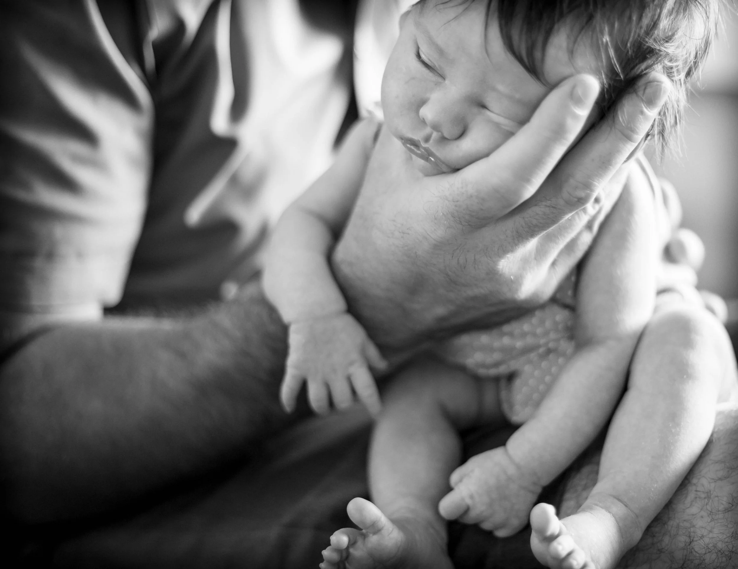 Black and white photo of a newborn baby cradled in a person's hand and arm, showing tender care.