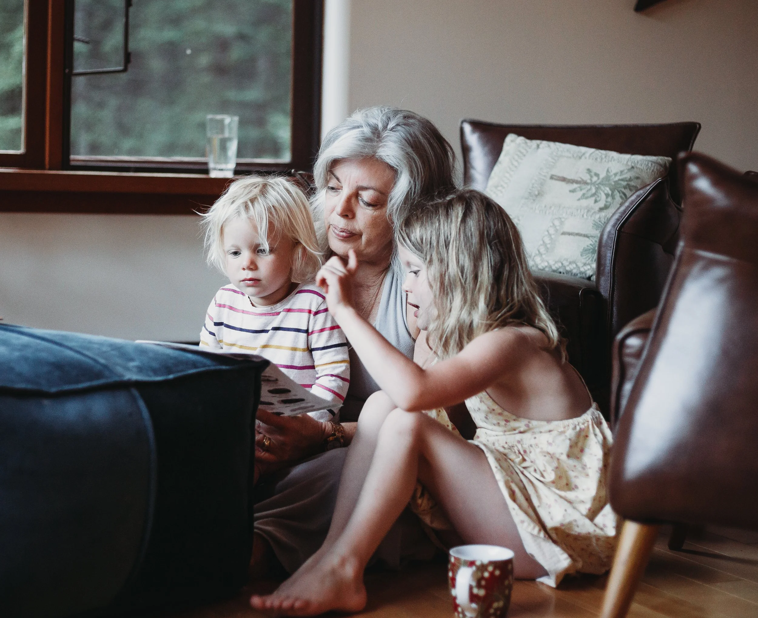 Grandmother reading a book with two young children in a cozy living room.
