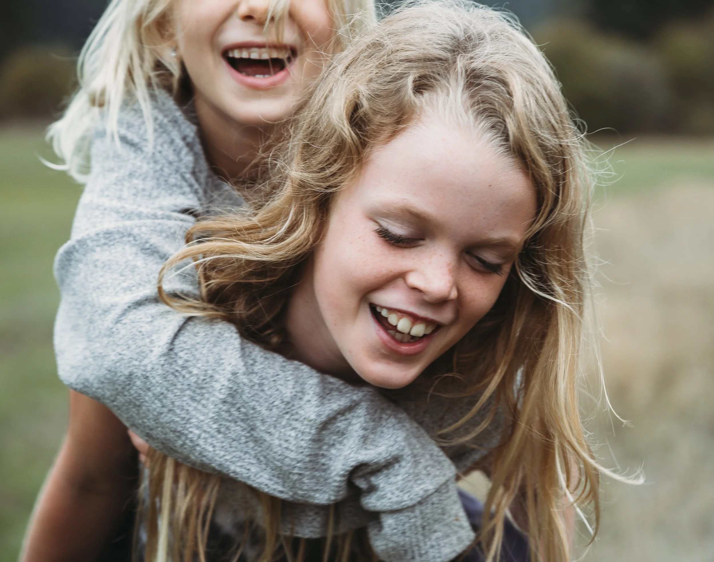 Two children playing outdoors, one giving a piggyback ride, both smiling and laughing.