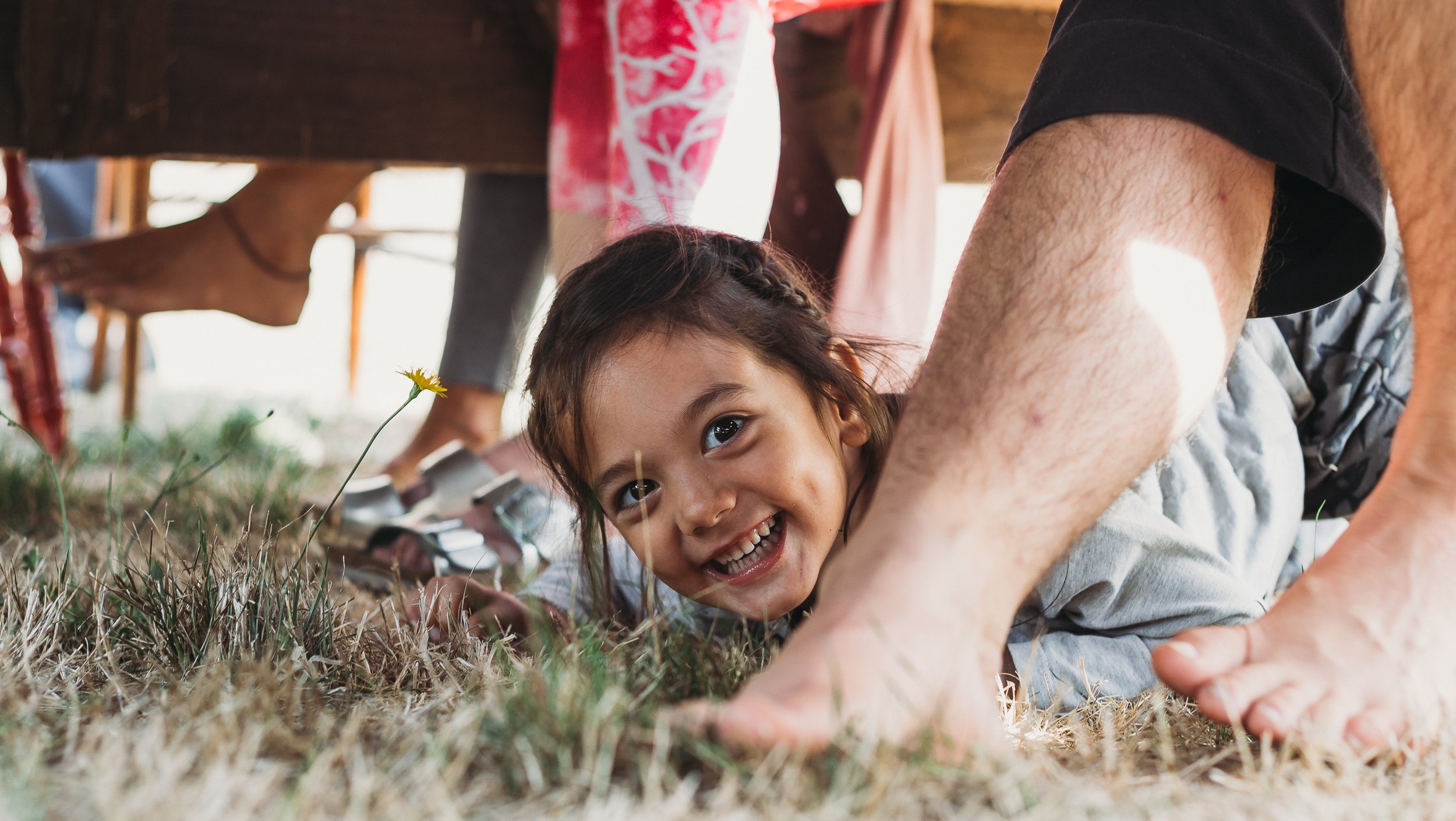 Child smiling under table with bare feet on grass