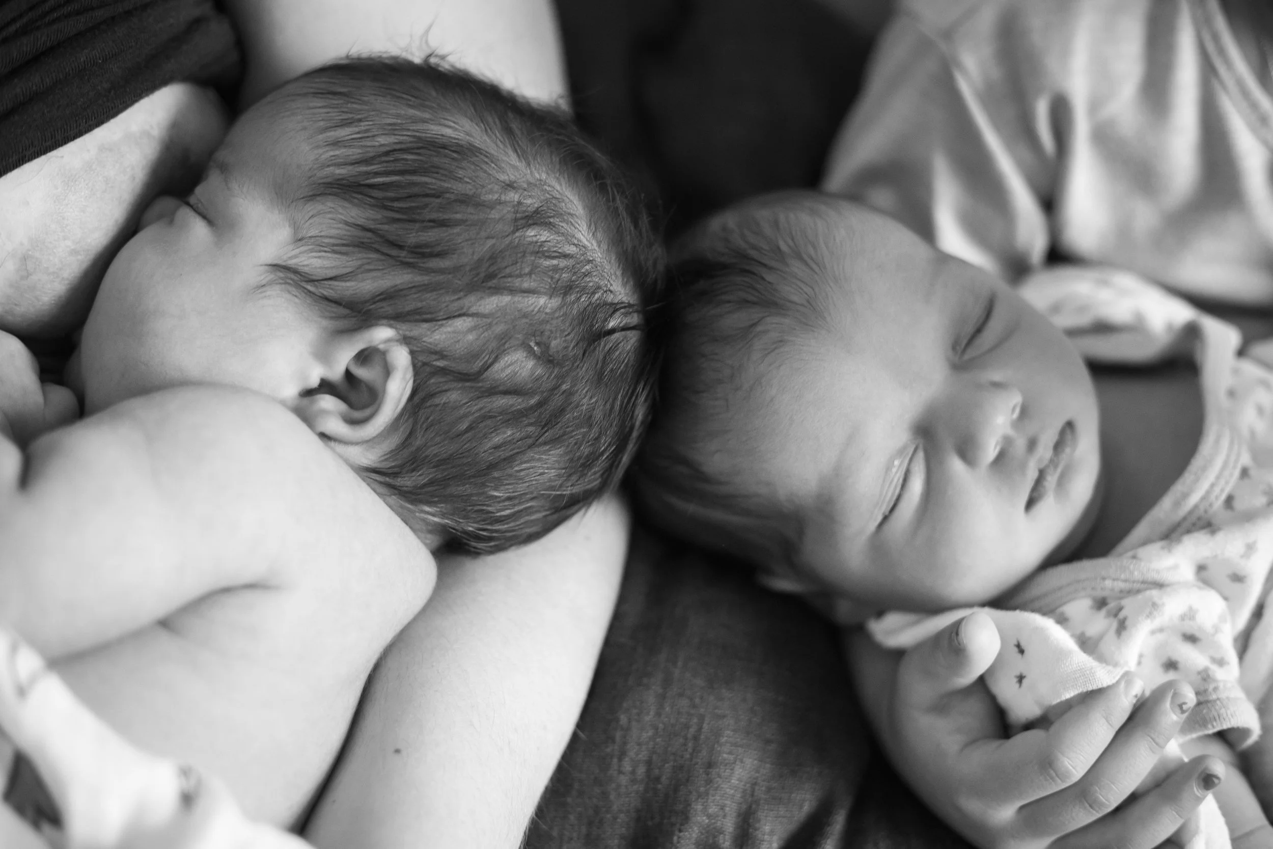 Black and white photo of two newborn babies sleeping closely together.