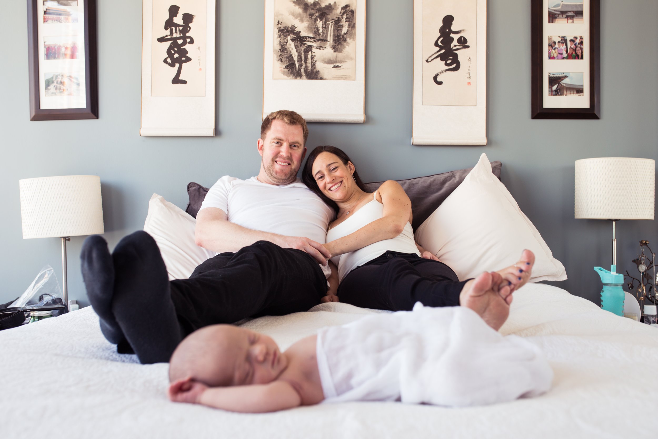 Family relaxing on bed with baby in foreground, decorative wall art in background.