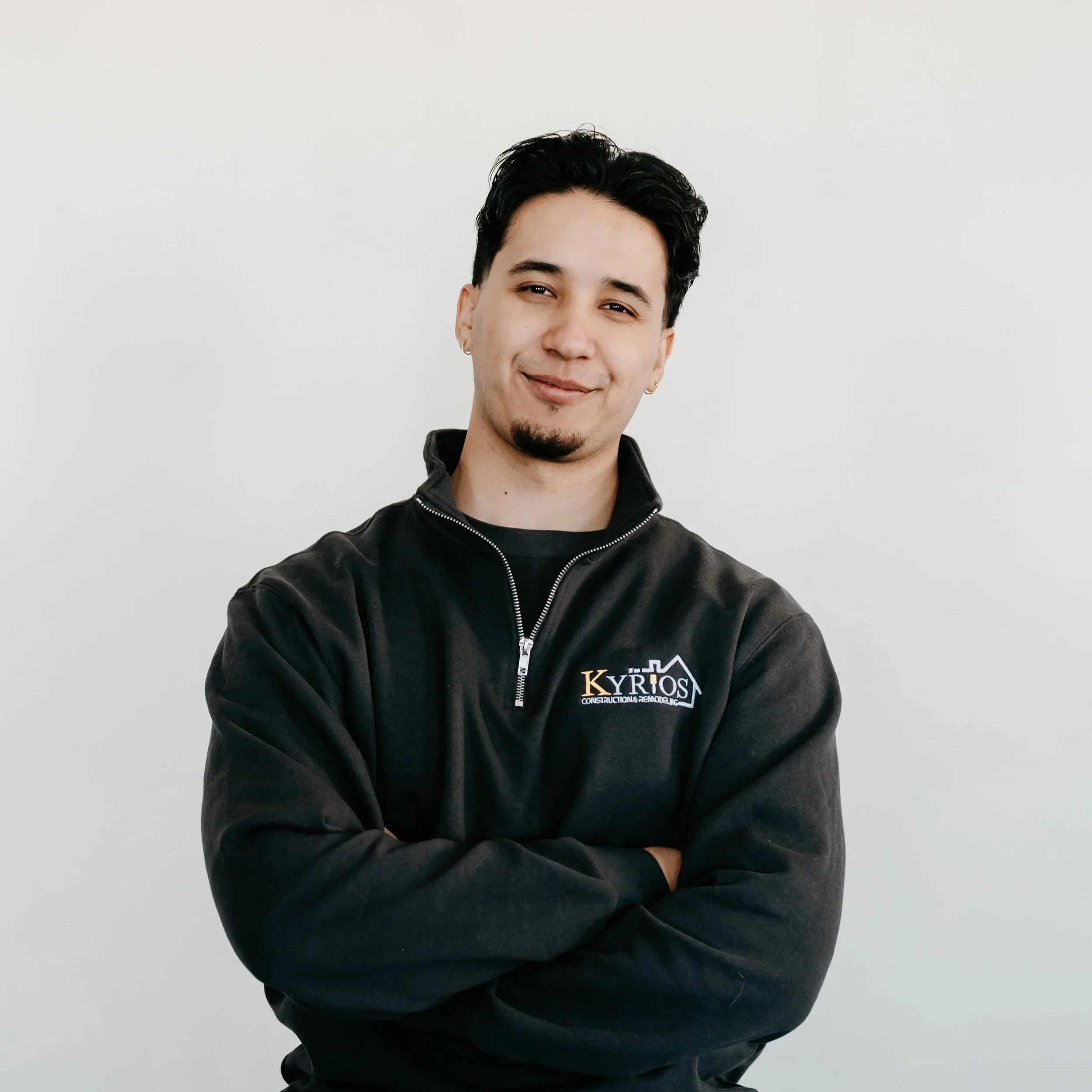 Smiling person wearing a dark t-shirt with arms crossed against a plain background.