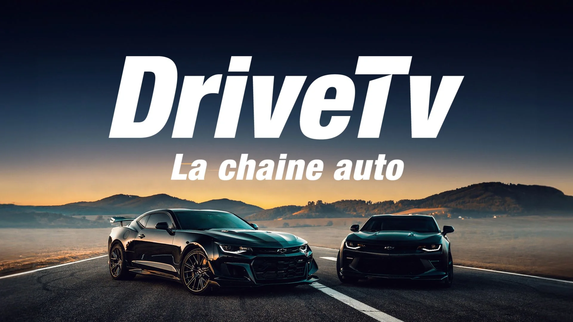 Deux voitures de sport noires sur une route au coucher du soleil avec un paysage de montagnes en arrière-plan et texte affiché en surimpression : 'DriveV La chaîne auto'.
