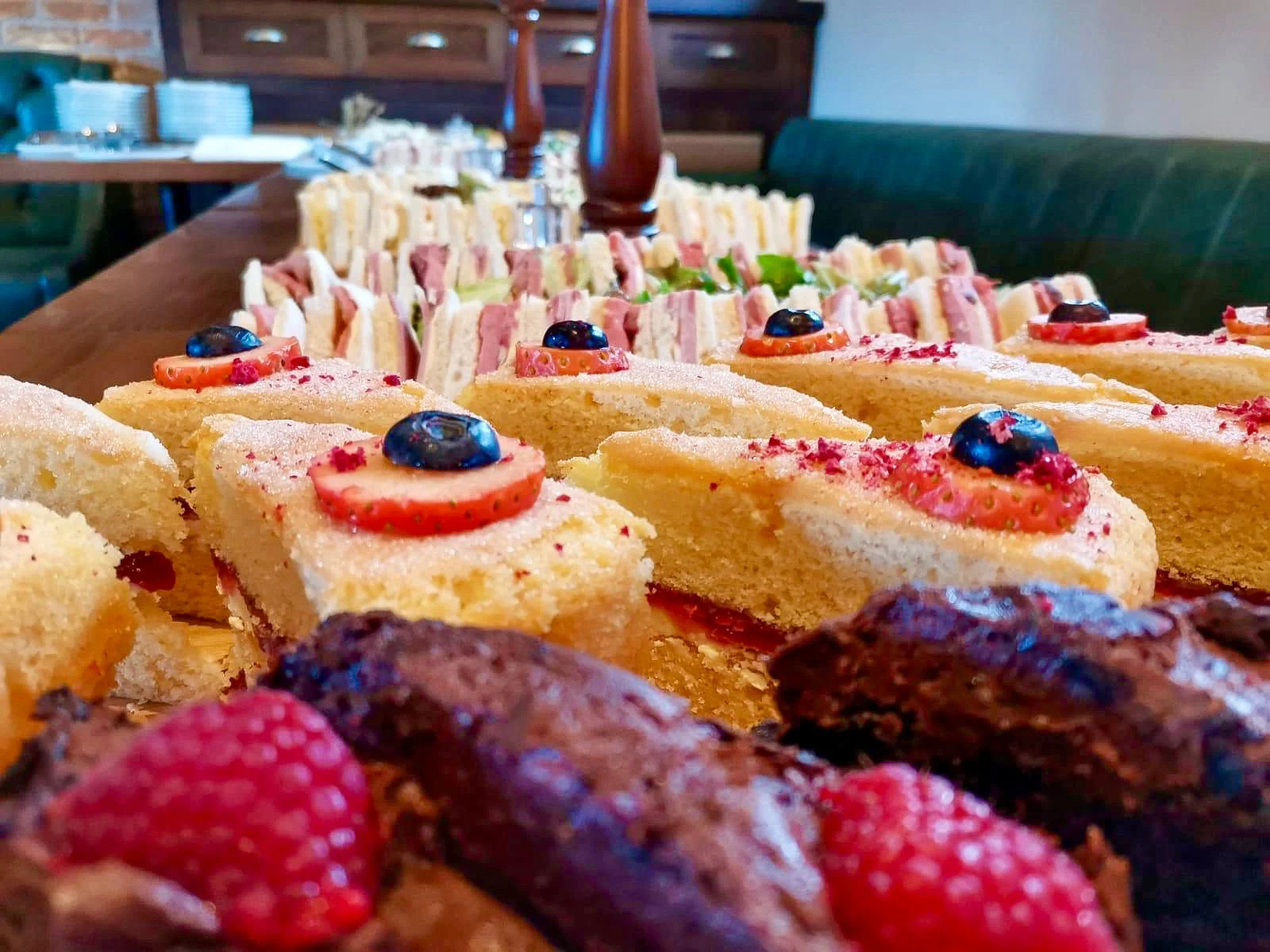 Assorted slices of cake and brownies topped with strawberries, blueberries, and red sprinkles, displayed on a wooden table.